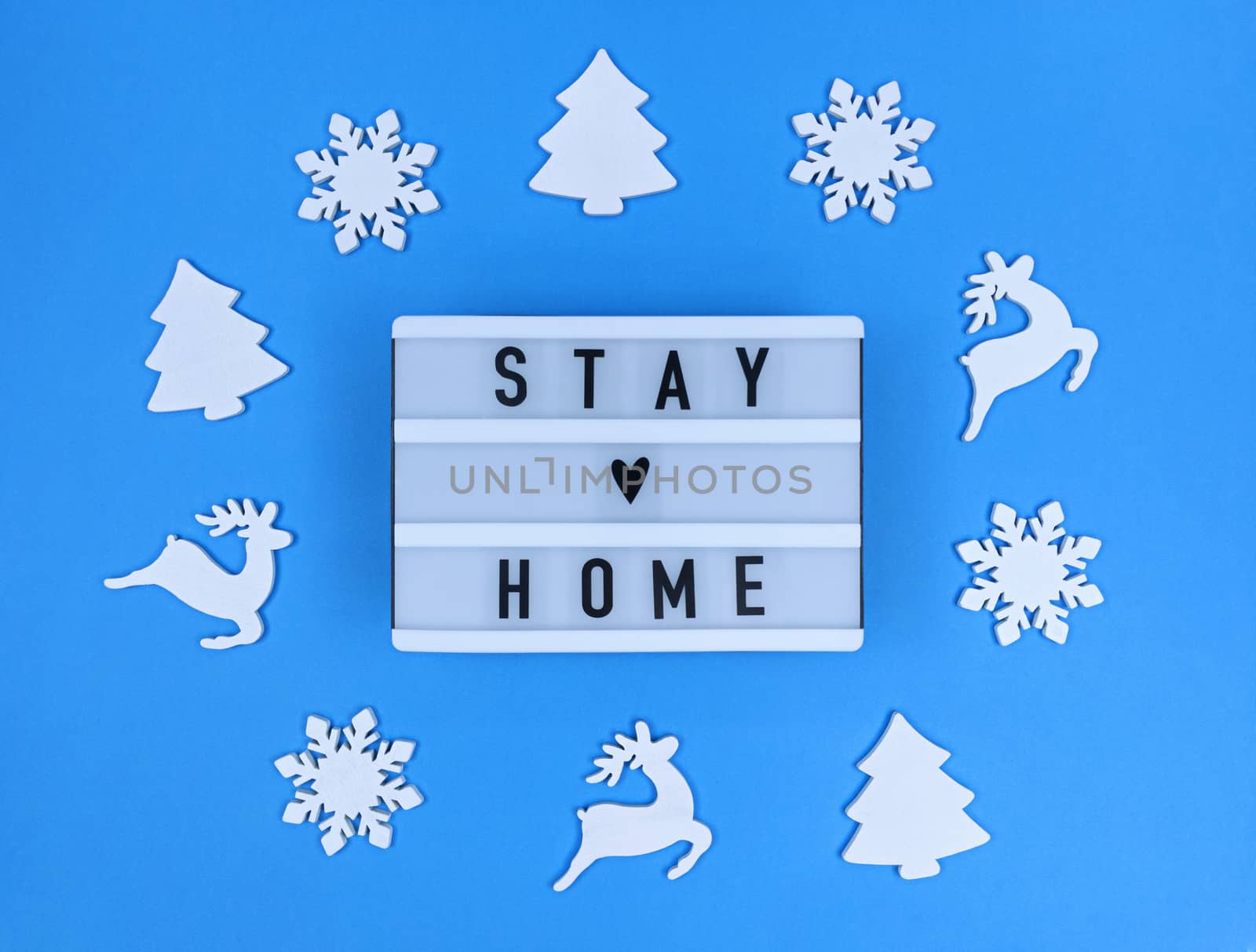 Light box with Stay home quote on blue background with christmas toys.