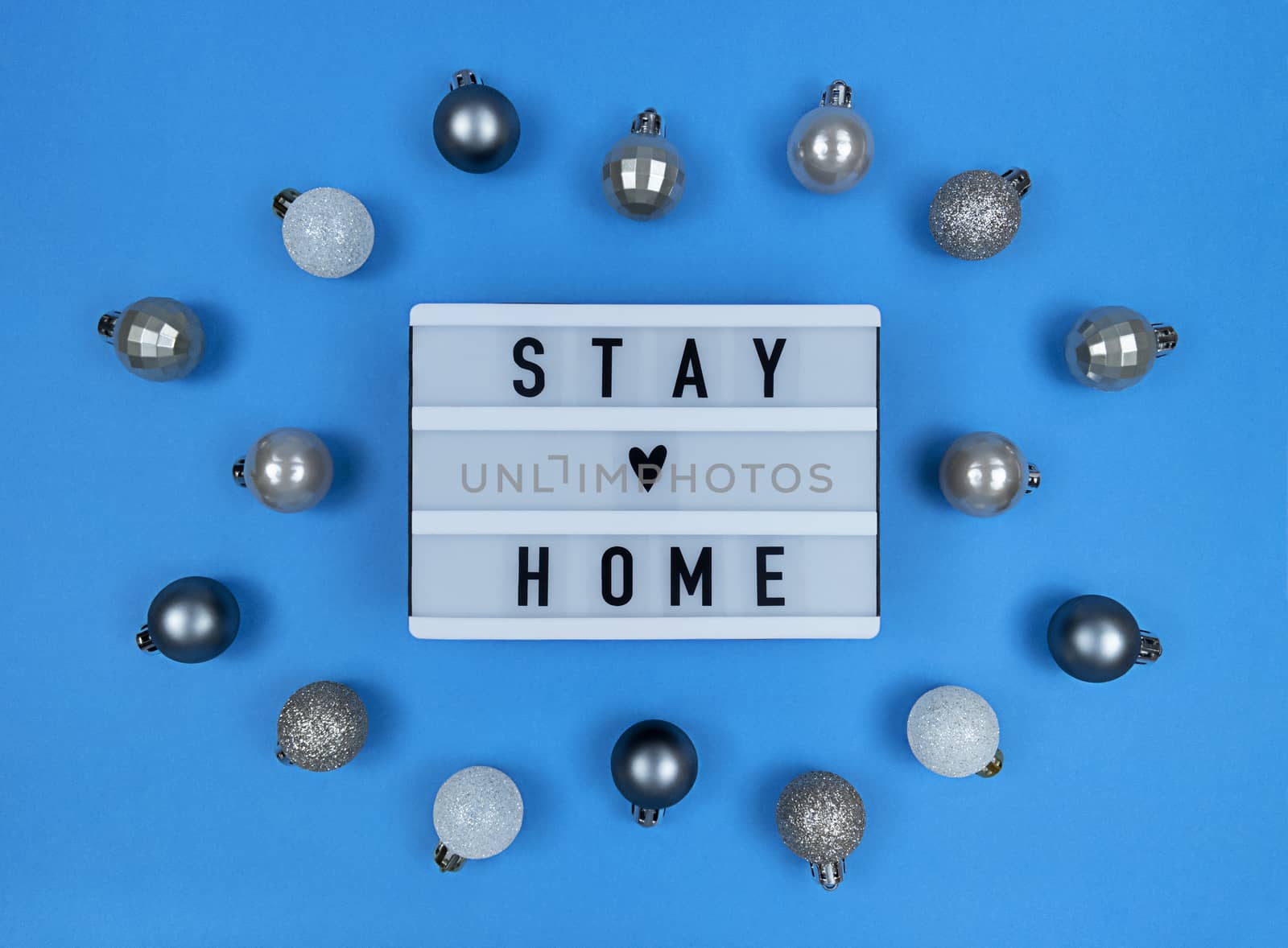 Light box with stay home quote on blue background with Christmas balls.