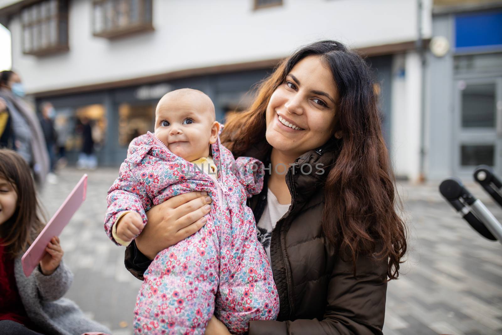 Happy beautiful mother smiling and holding cute baby daughter in pink jumpsuit. Joyful mother hugging baby outside. Young family fun day outdoors