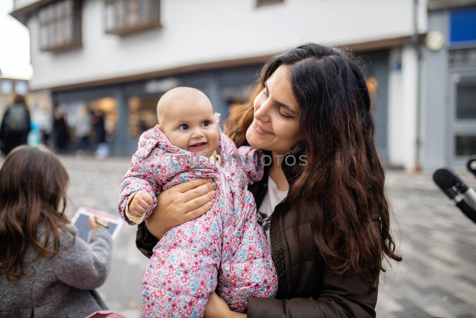 Happy beautiful mother smiling and holding cute baby daughter in pink jumpsuit. Joyful mother hugging baby outside. Young family fun day outdoors