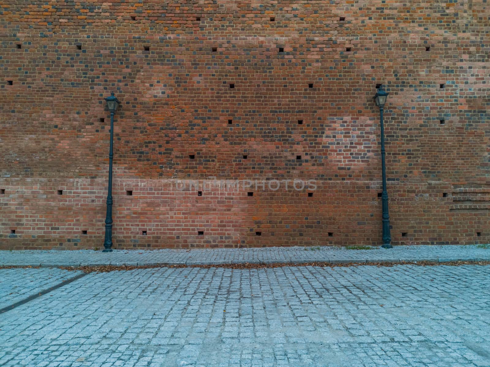 Red brick wall with two high black lamps near pavement