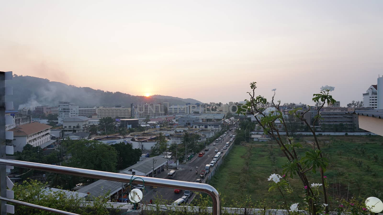 Drone view of the city of Patong, Phuket island. Houses of different heights stand on the beach. Green hills of the island. On the roof of houses pools, people swim. On the road go scooters and cars.