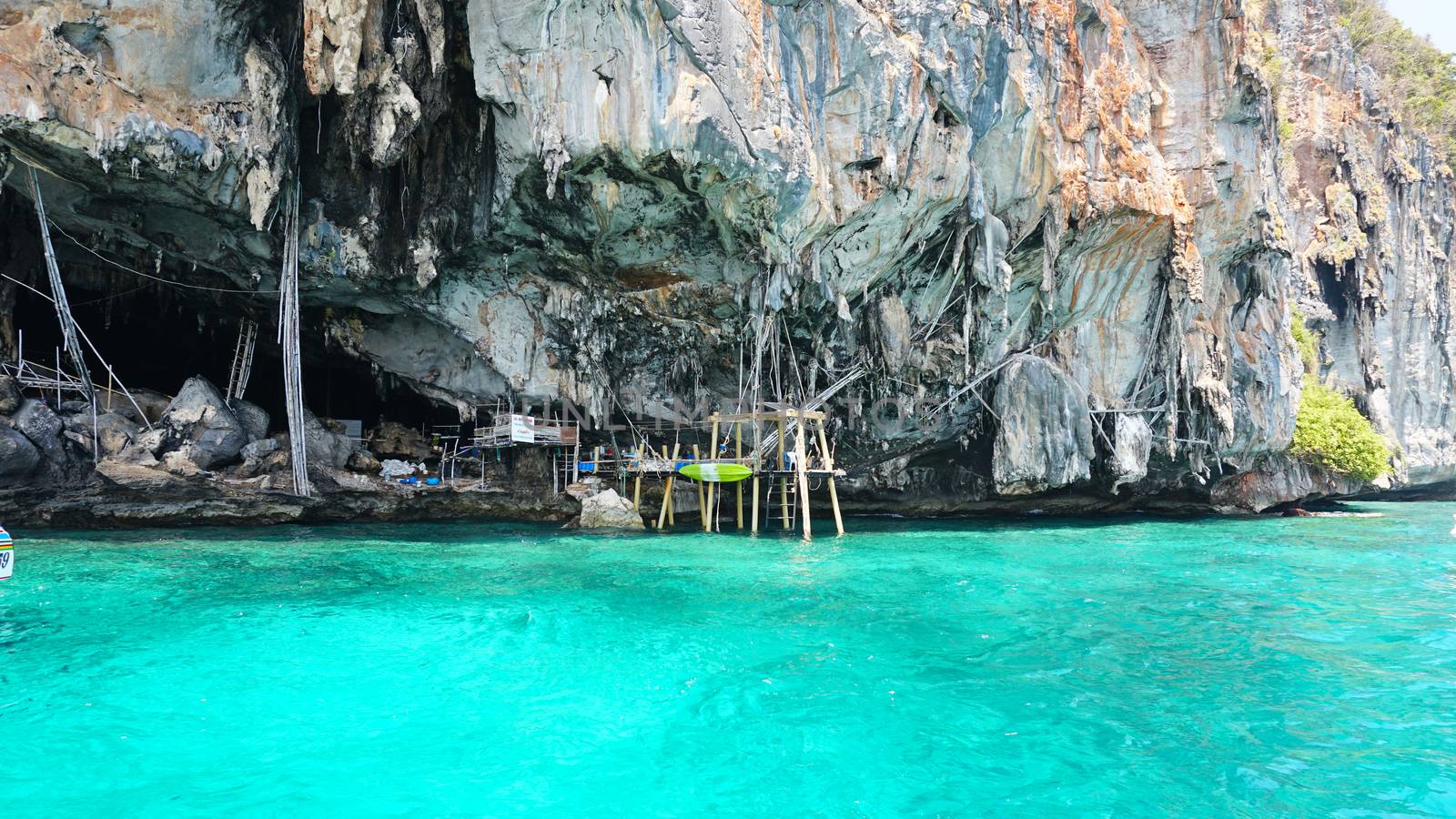 A large cave with hanging stalactites. Viking cave in Thailand. Turquoise clear water. Large blocks of gray stones. A small Bush grows. The entrance from the ocean. Unusual place.