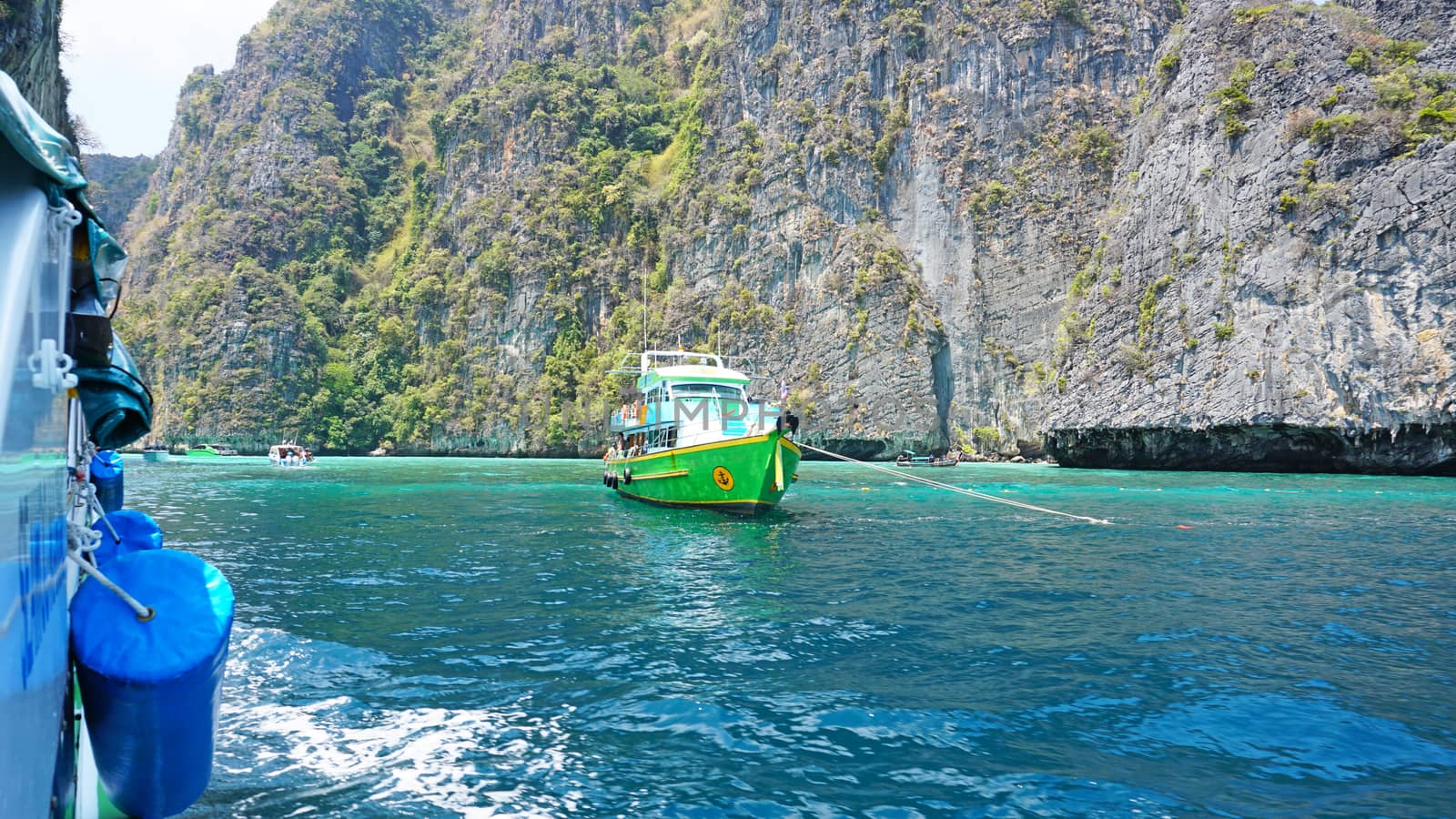 Blue water, green hills and steep rocks. The boat sails near the island. Boat with tourists in the Bay. Steep cliffs and caves. Group of tourists on the boat. Sea excursion. Water gradient.