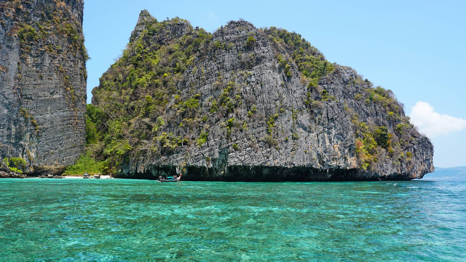 Blue water, green hills and steep rocks. The boat sails near the island. Boat with tourists in the Bay. Steep cliffs and caves. Group of tourists on the boat. Sea excursion. Water gradient.