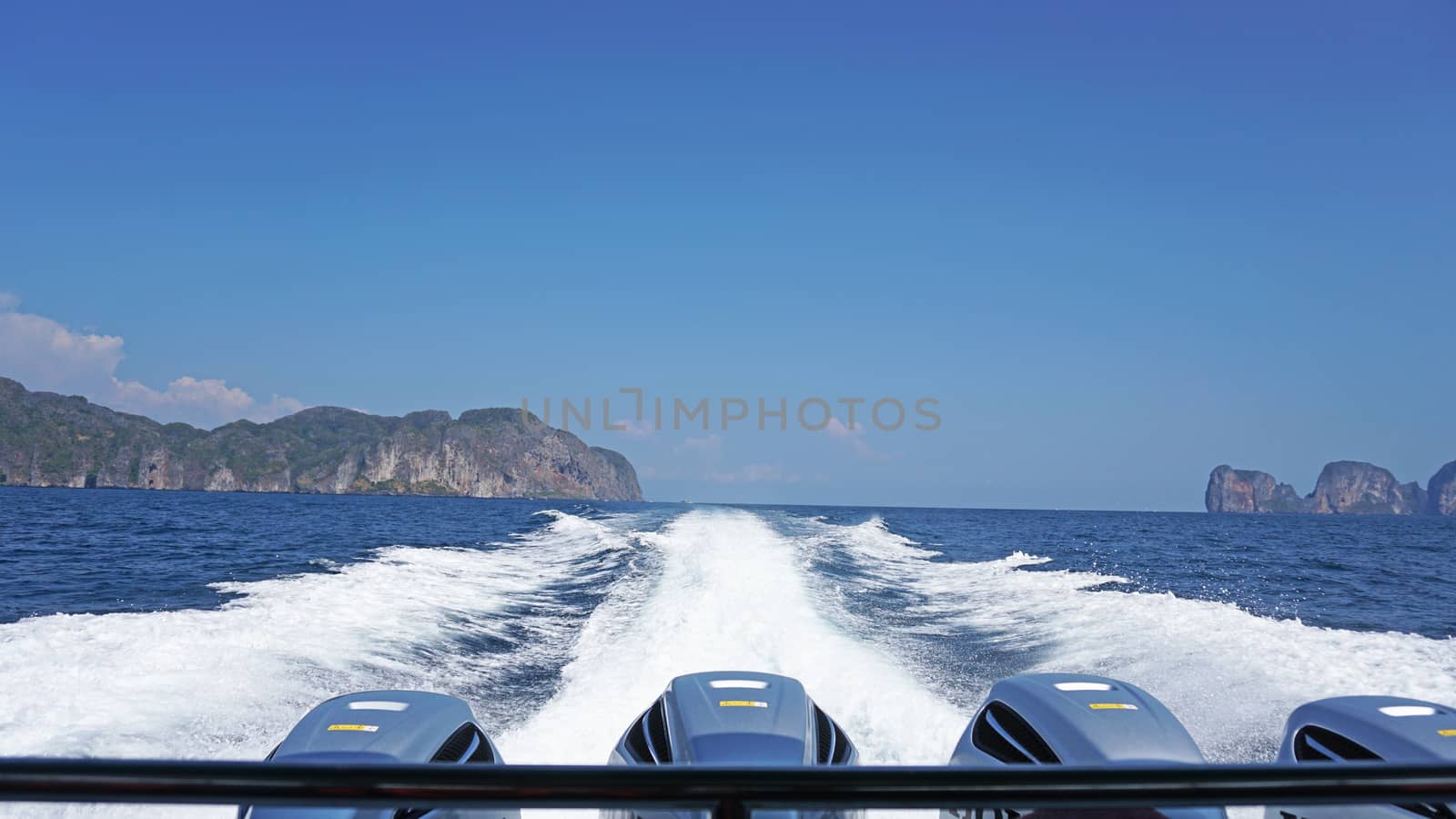 Waves from the engines of a high-speed boat. Rear view. Blue sky, white cloud and far island. White foam from waves. Floating in the ocean.