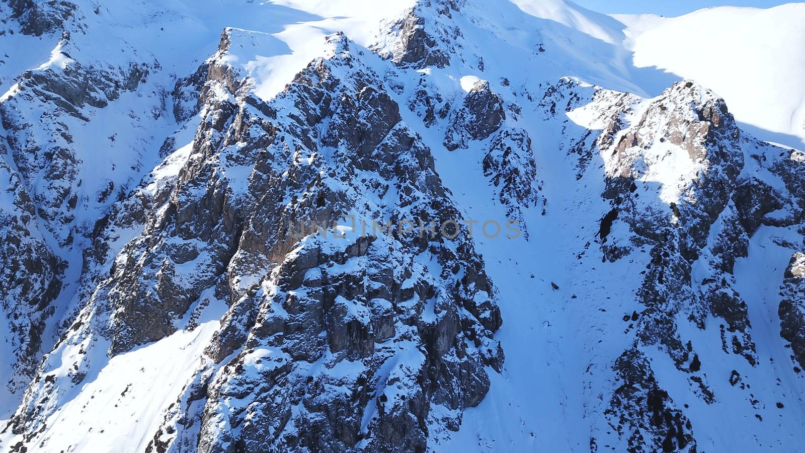 Huge rocks covered with snow. Dangerous terrain. High mountains, cliffs, and large rocks. Shadow from the sun's rays. Top and side view from the drone. An epic place. The Mountains Of Almaty.