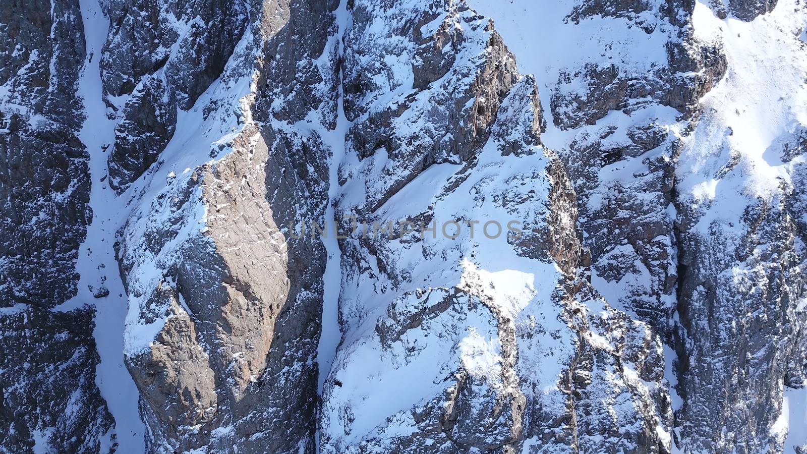 Huge rocks covered with snow. Dangerous terrain. High mountains, cliffs, and large rocks. Shadow from the sun's rays. Top and side view from the drone. An epic place. The Mountains Of Almaty.