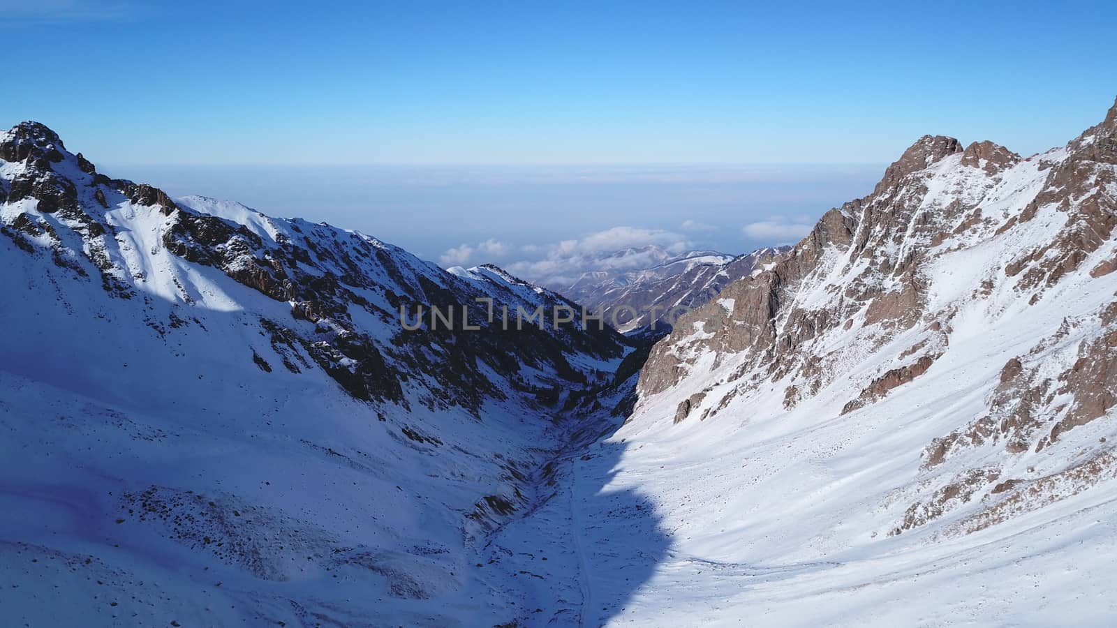 Snow mountain peaks with rocks. View from drone. In places, you can see glaciers, large rocks and rocks. Huge drifts of snow covered mountains. Dangerous place. Blue sky and sun. Shadow of the peaks.