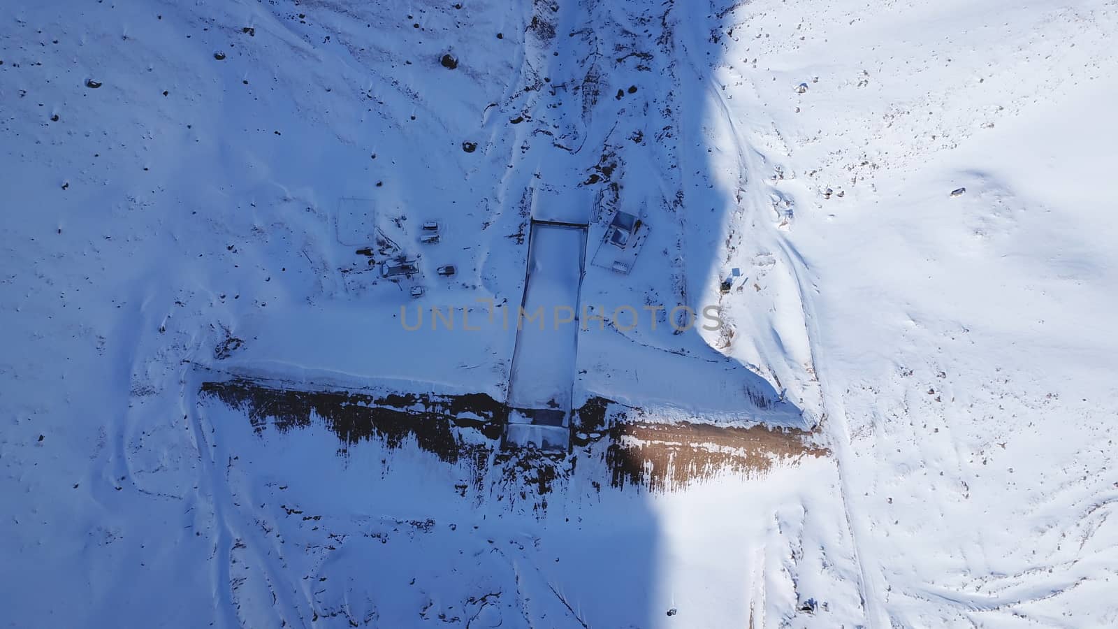 The dam was covered with snow in the mountains. The view from the top. The river is frozen, everything is covered with snow. Equipment, houses, a gorge in the snow. Shadow from the sun. Mountain dam.