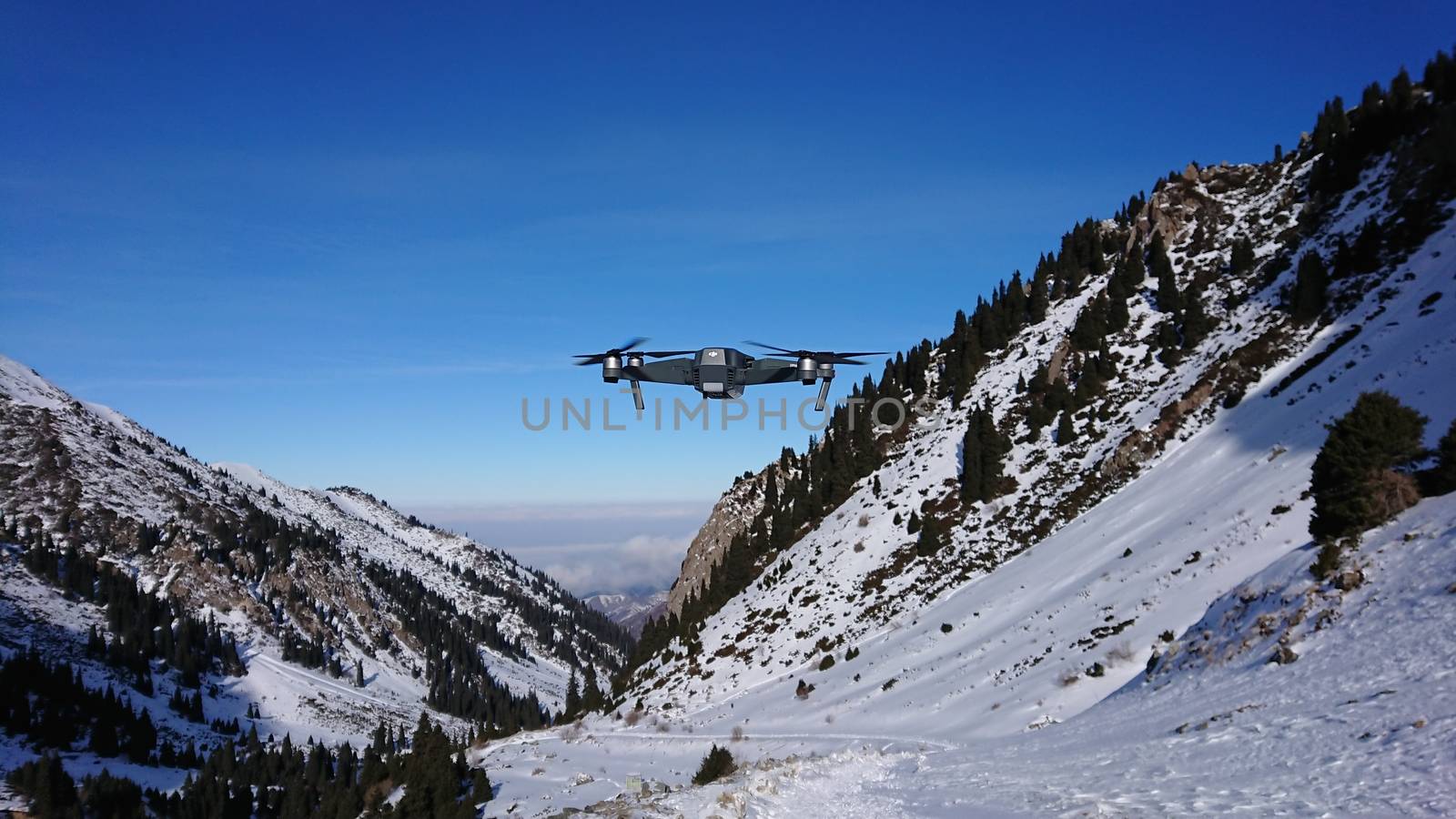 DJI Mavic Pro in the air in the winter gorge. A professional quadcopter takes pictures of nature. Mountainous terrain, winter, lots of snow. Pine trees grow on the rocks. The Mountains Of Almaty.