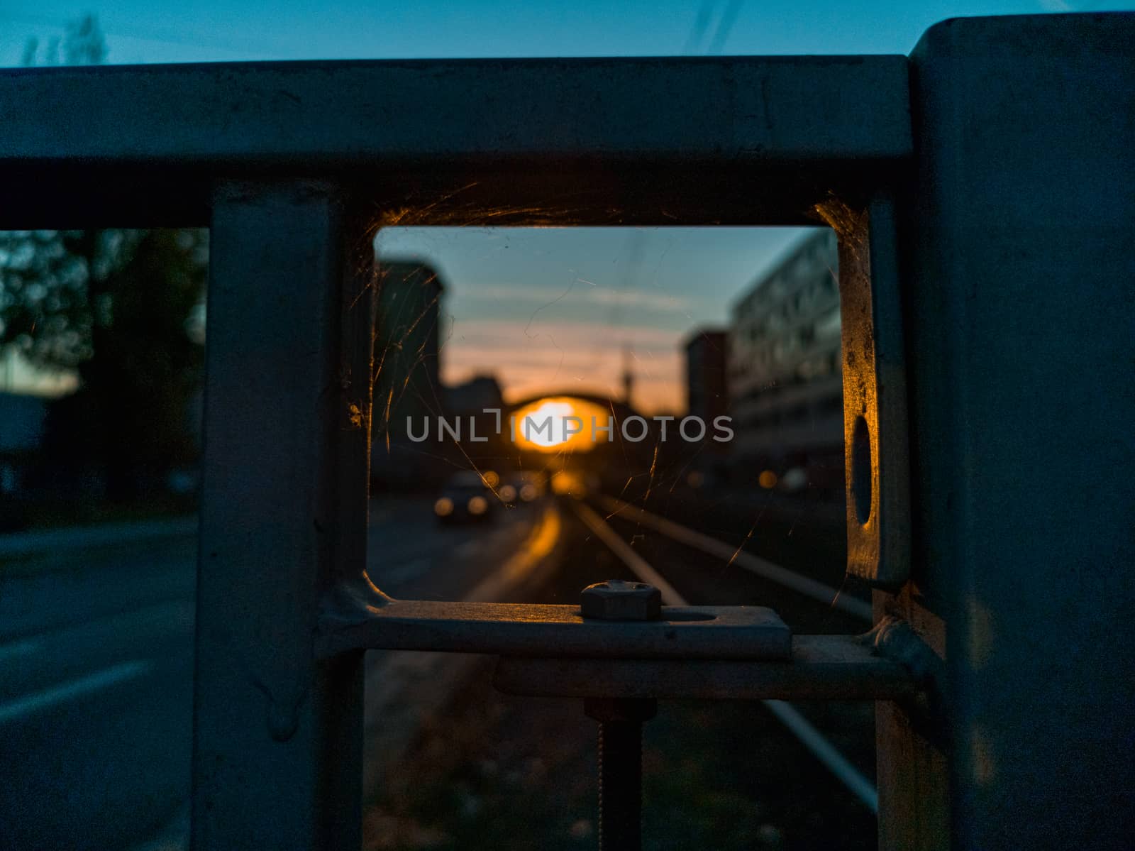 Spider's net inside metal barrier in front of sunset over street