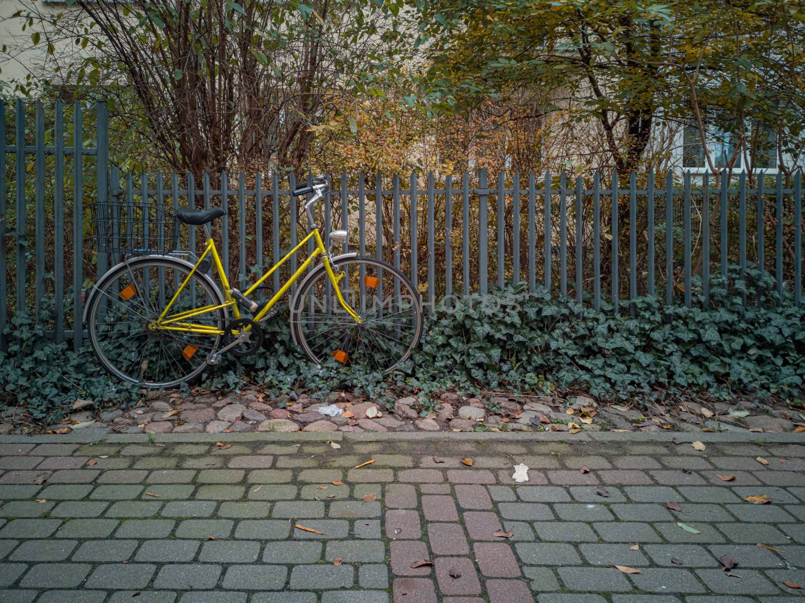 Old yellow bicycle leaning against the metal fence