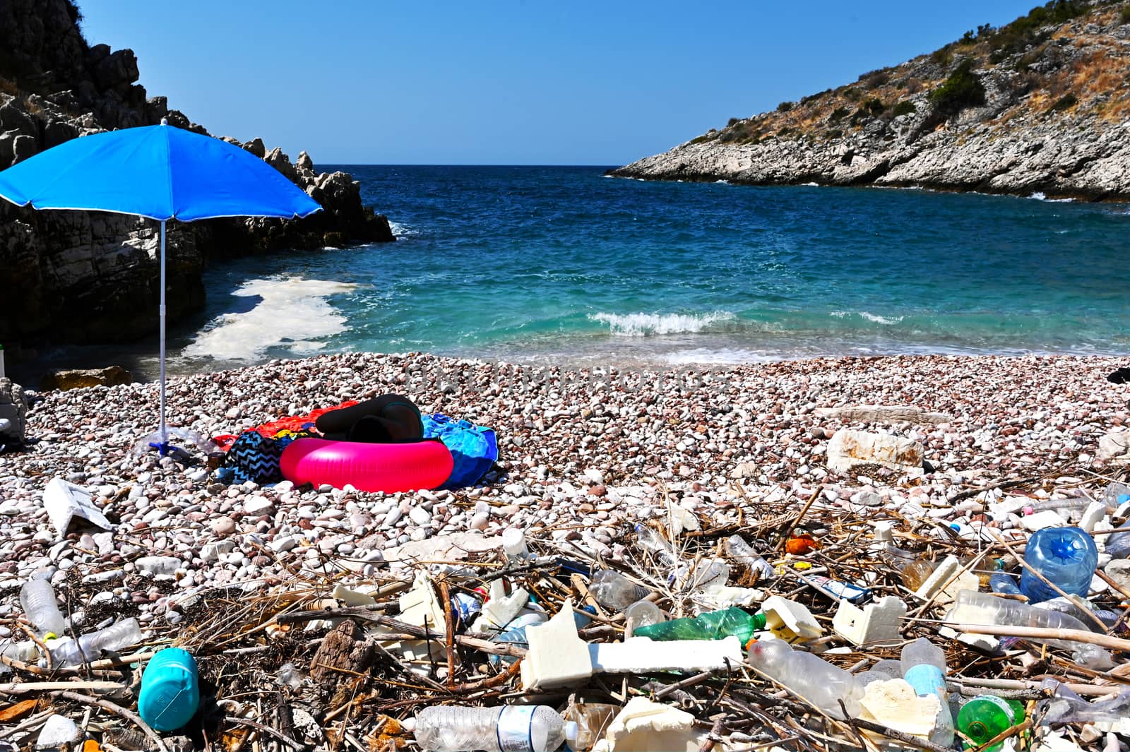 Dirty beach of Albania coast with girl sleeping in background. Empty, used dirty plastic bottles. Environmental pollution. Ecological problem.