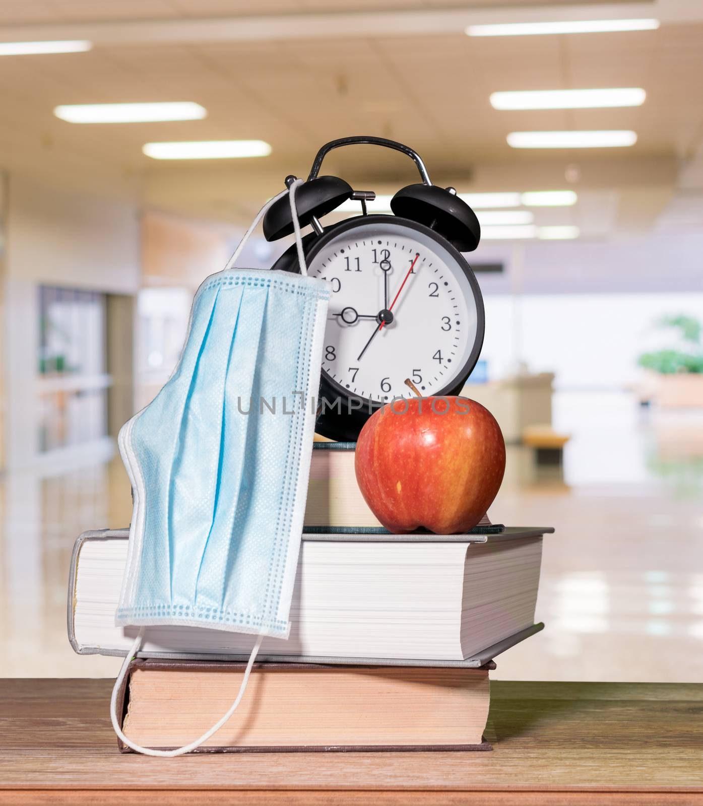 Back to school background concept with stack of books, alarm clock, apple with face mask by steheap