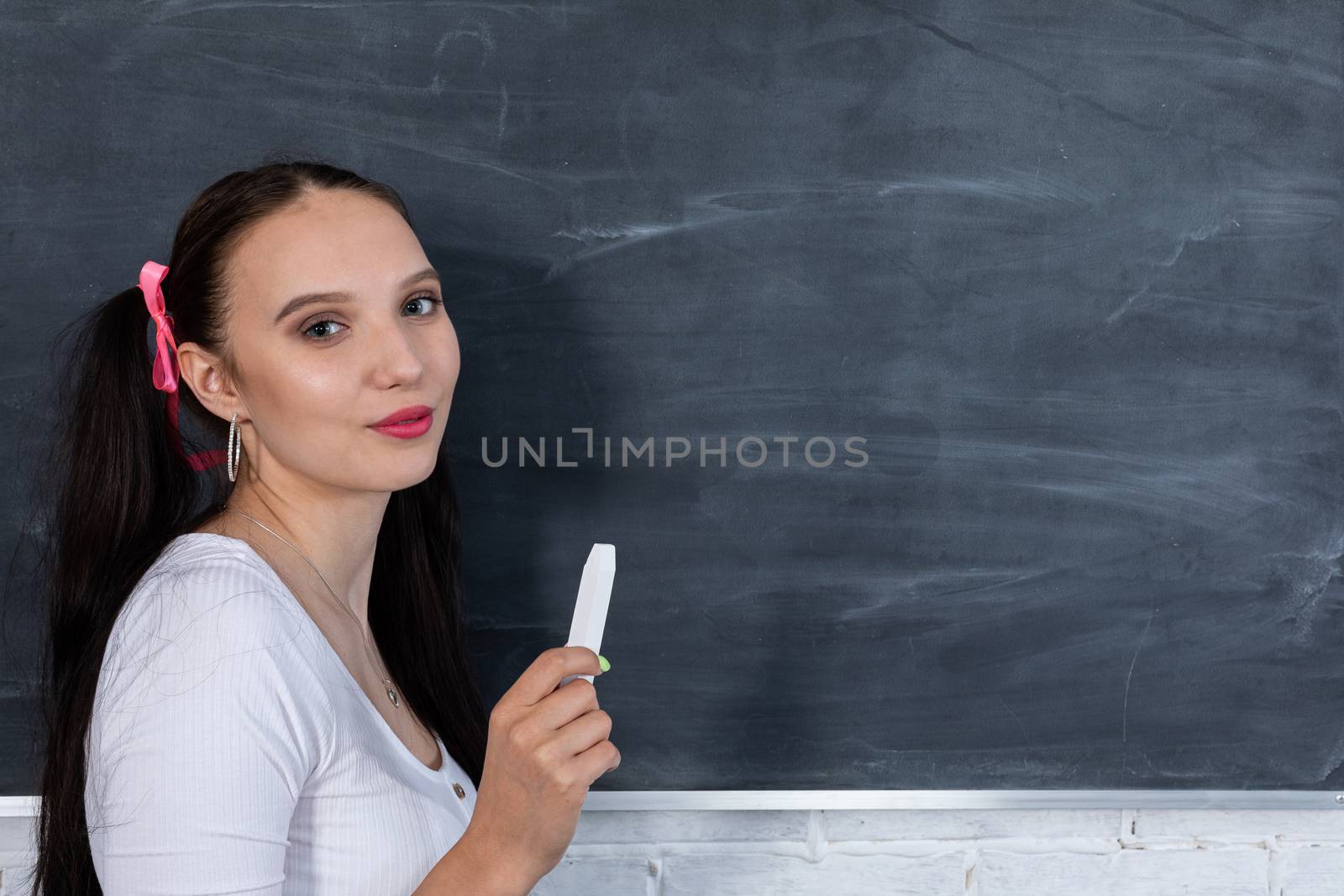 A teenager stands and looks straight into the lens. The girl has long dark hair tied with pink bows on both sides of her head.