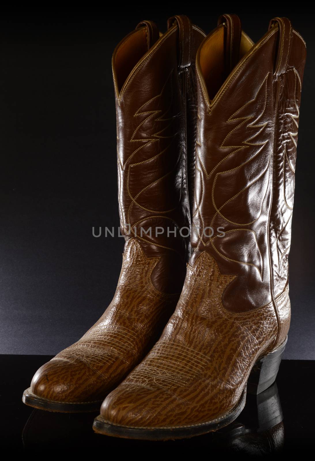A pair of leather cowboy boots over a black reflective background.