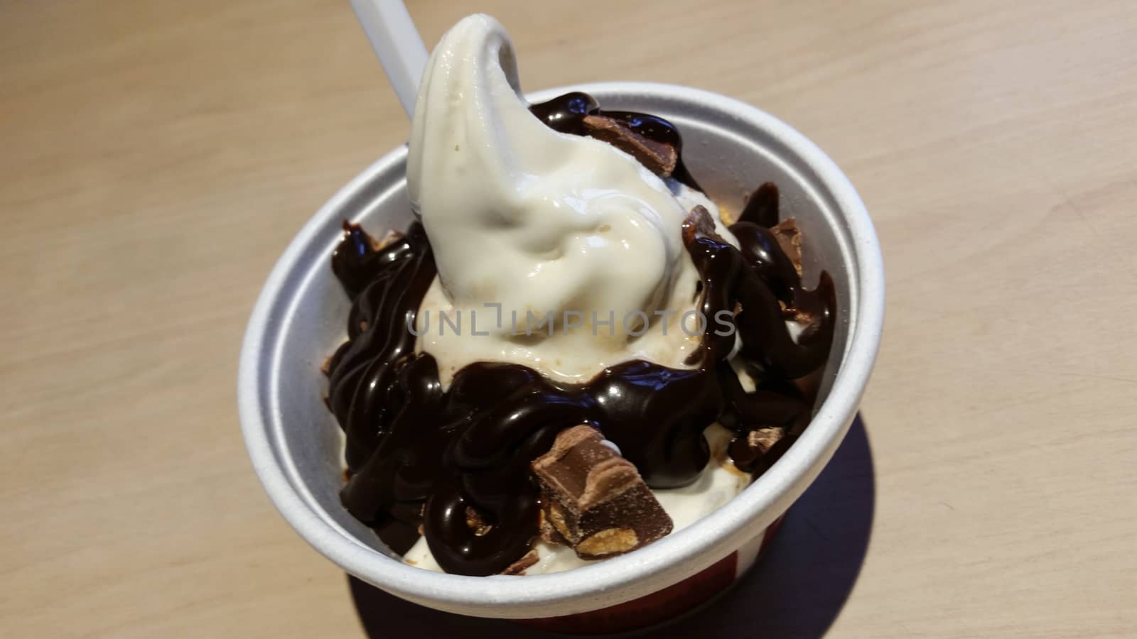 Bowl of vanilla ice cream with cream of chocolate on white wooden background. From top view