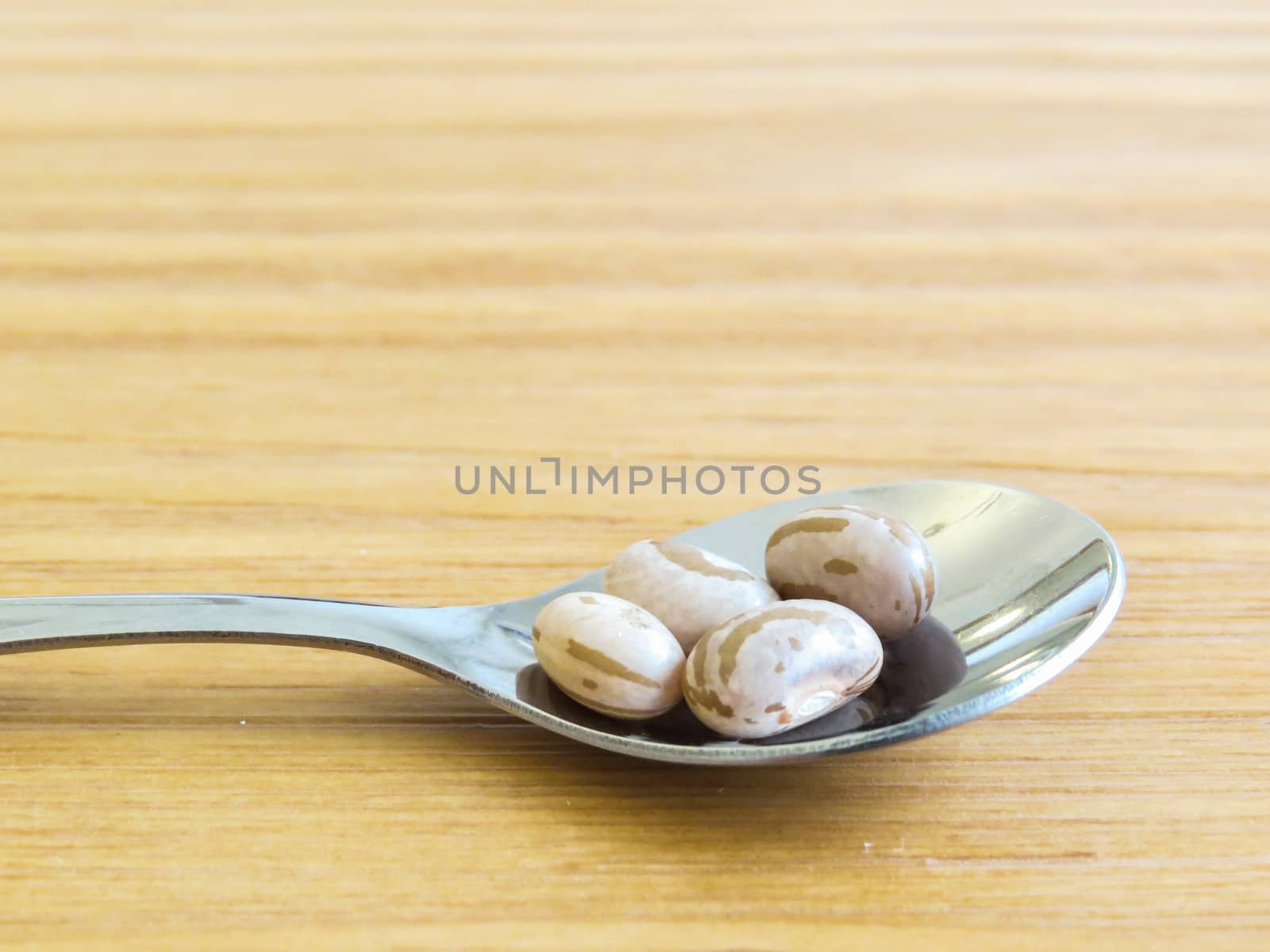 Closeup of polished steel spoon with carioca beans on wooden board.