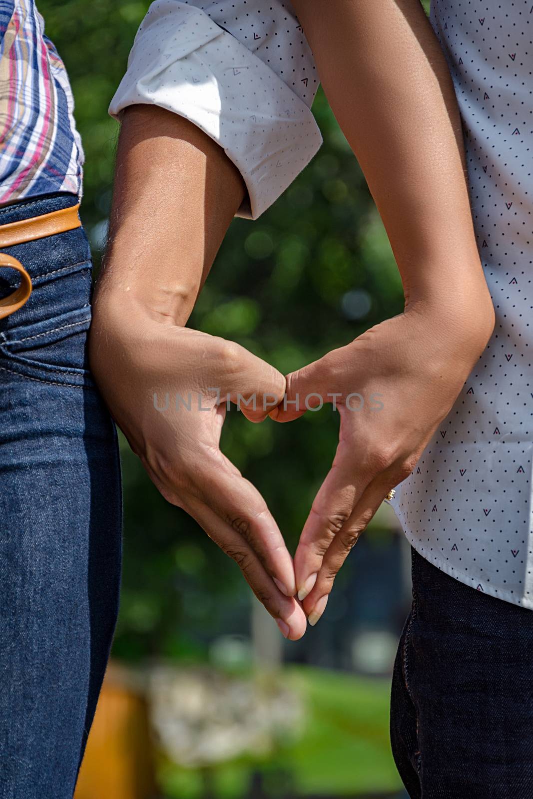 wedding couple holding hands in a heart shape, with the background of a park