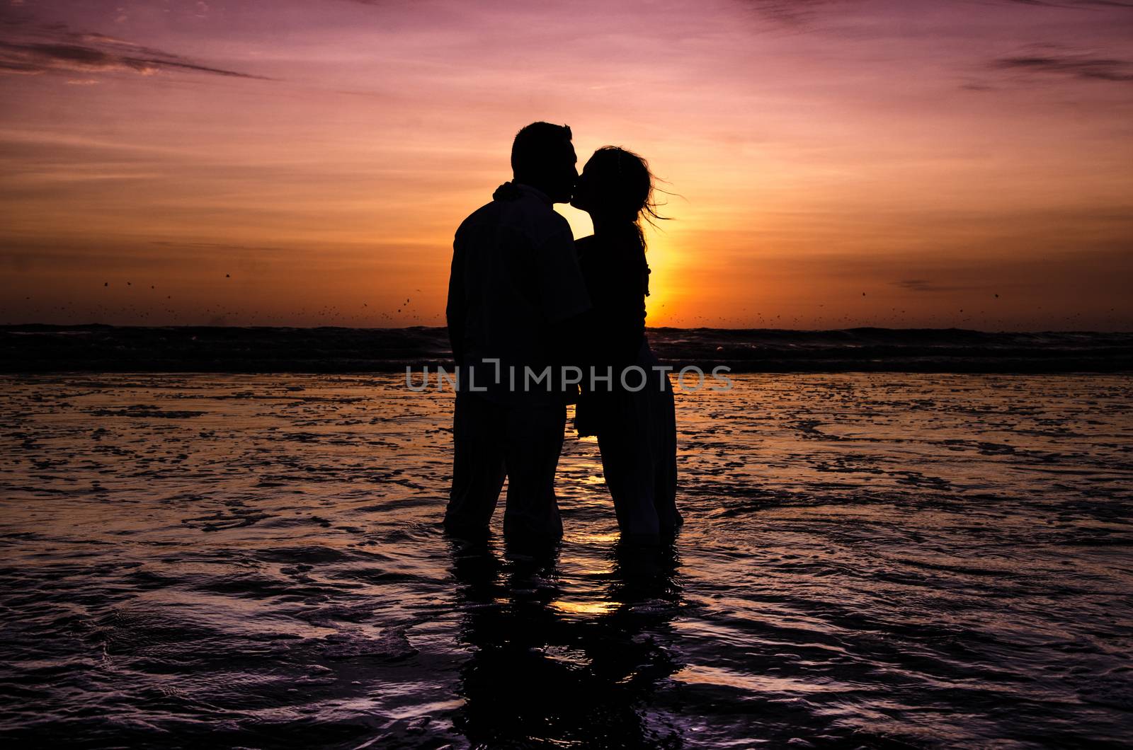 silhouettes in love romantic couple lovers hugging, kissing, touching, eye contact at sunset, sunrise on the background of the sea, the sun, the clouds in fiery red, orange colors