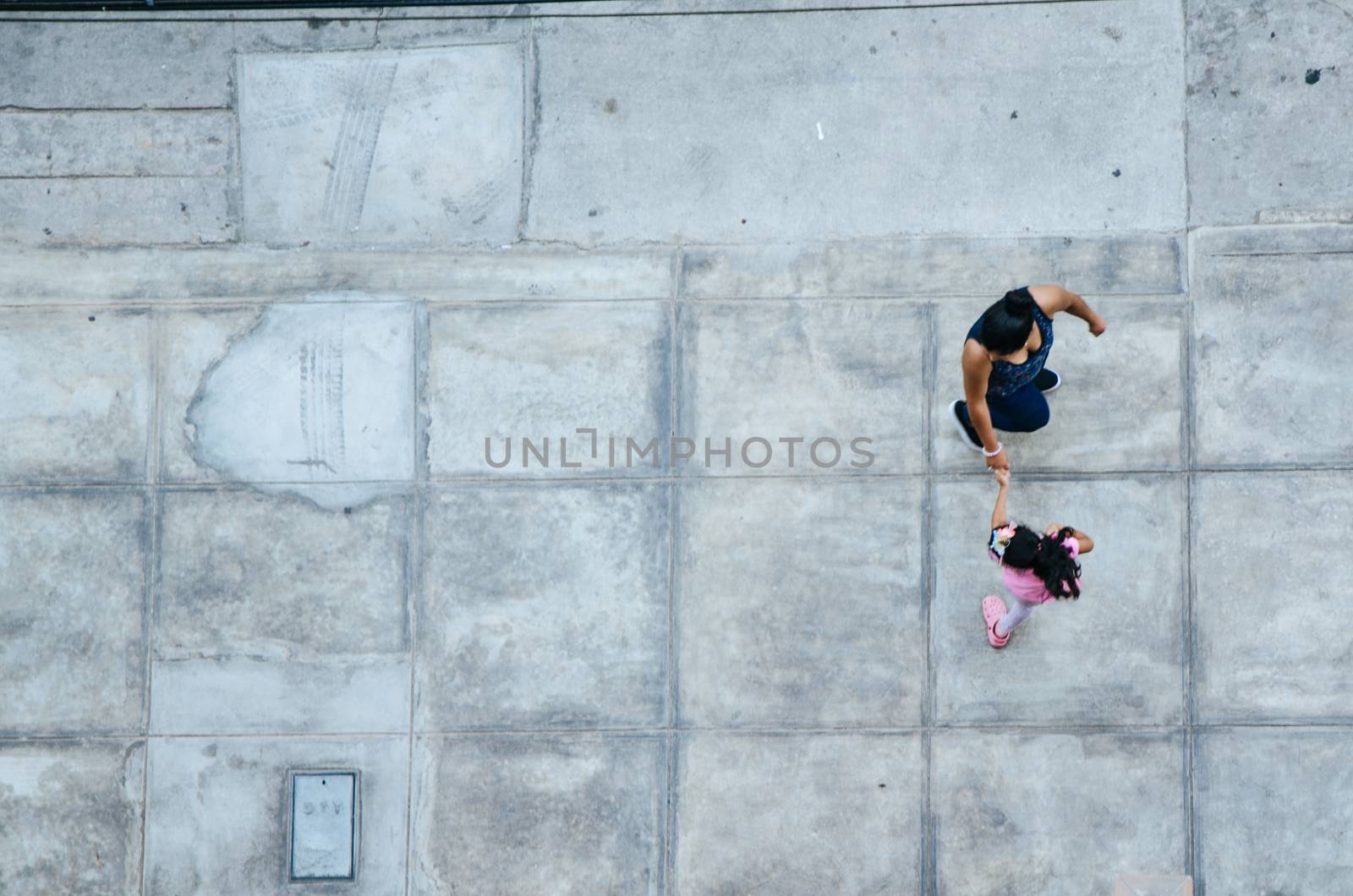 Mother and daughter walking on the pavement. View from above
