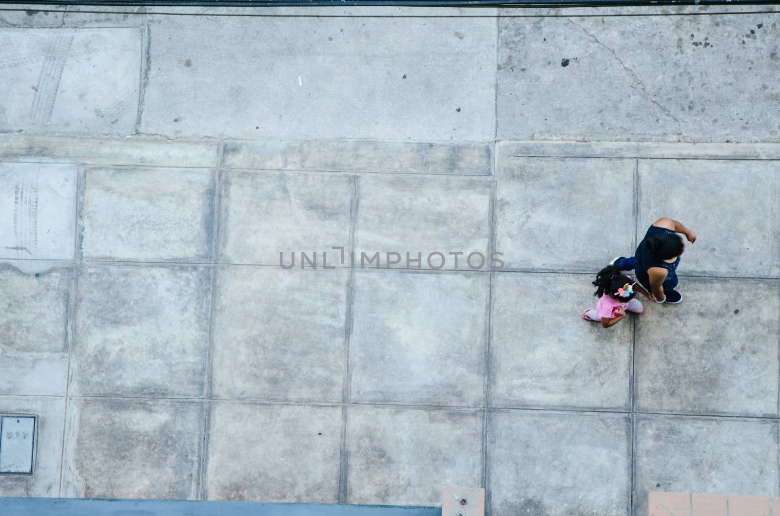 Mother and daughter walking on the pavement. View from above