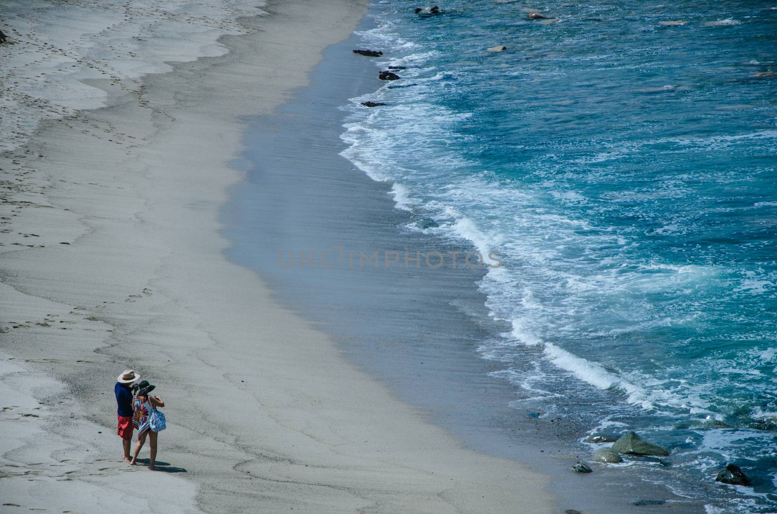 A couple, man and woman, on the shore of a beach taking pictures
