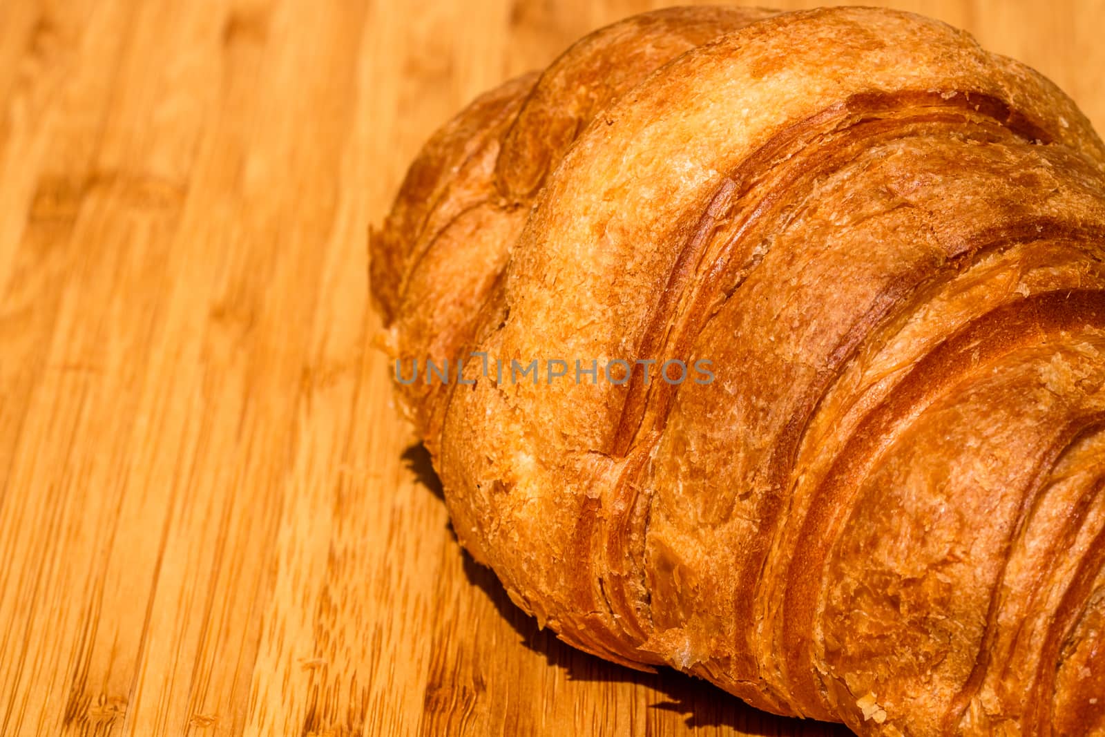 Detail of fresh croissant on wooden table. Food and breakfast concept. Close up photo of French buttery croissant