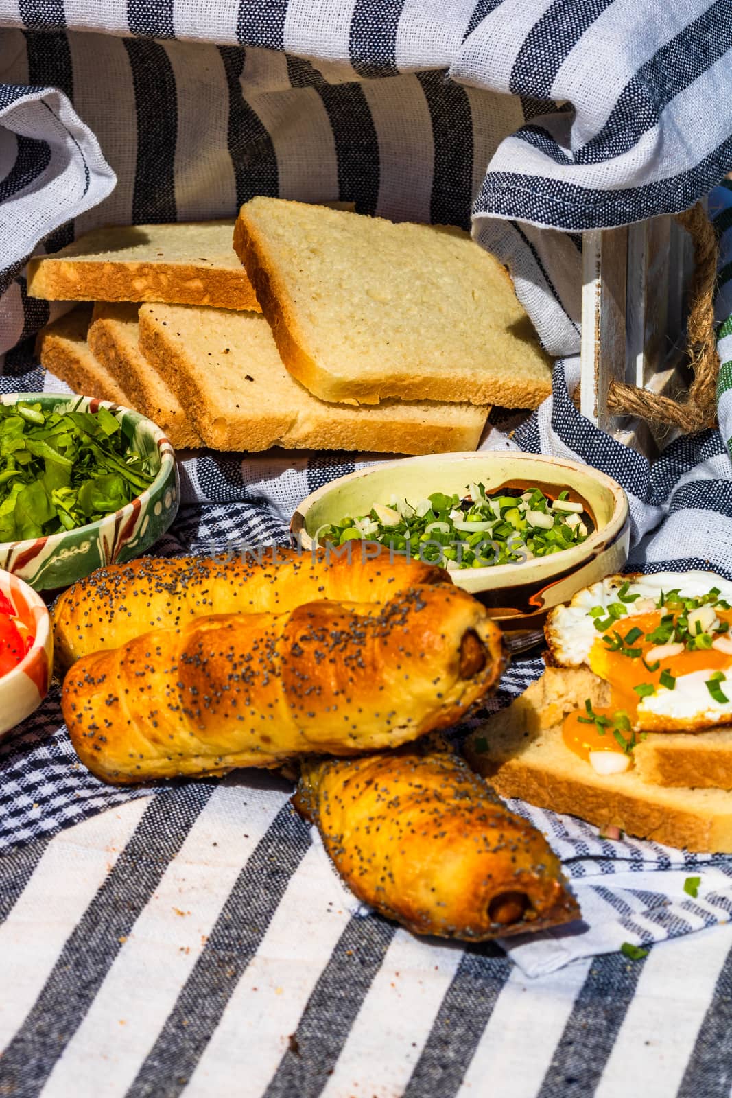 Rustic composition with sausages rolls, fried egg on toast bread, different bowls with sauce and chopped vegetables.