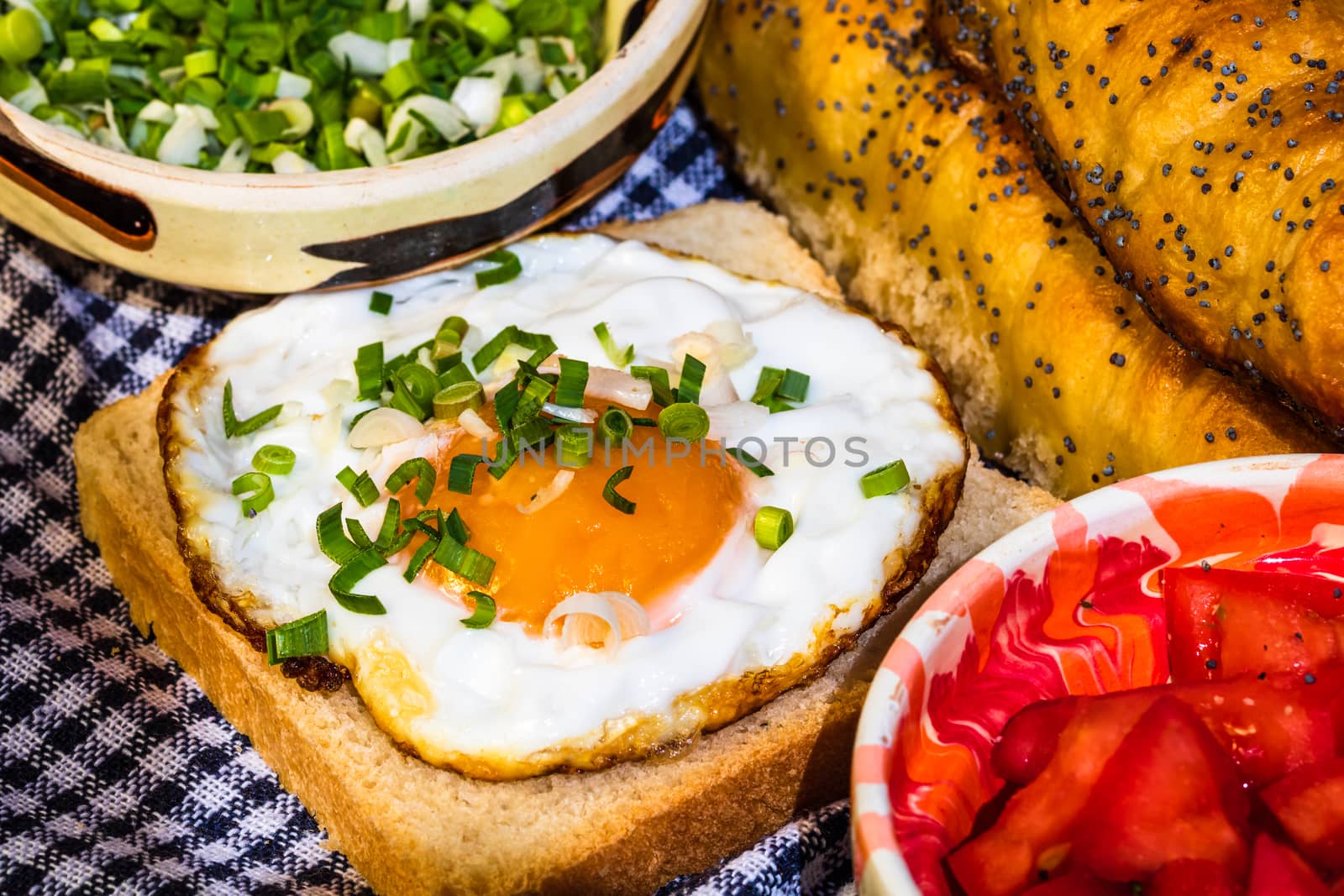 Rustic composition with sausages rolls, fried egg on toast bread, different bowls with sauce and chopped vegetables.