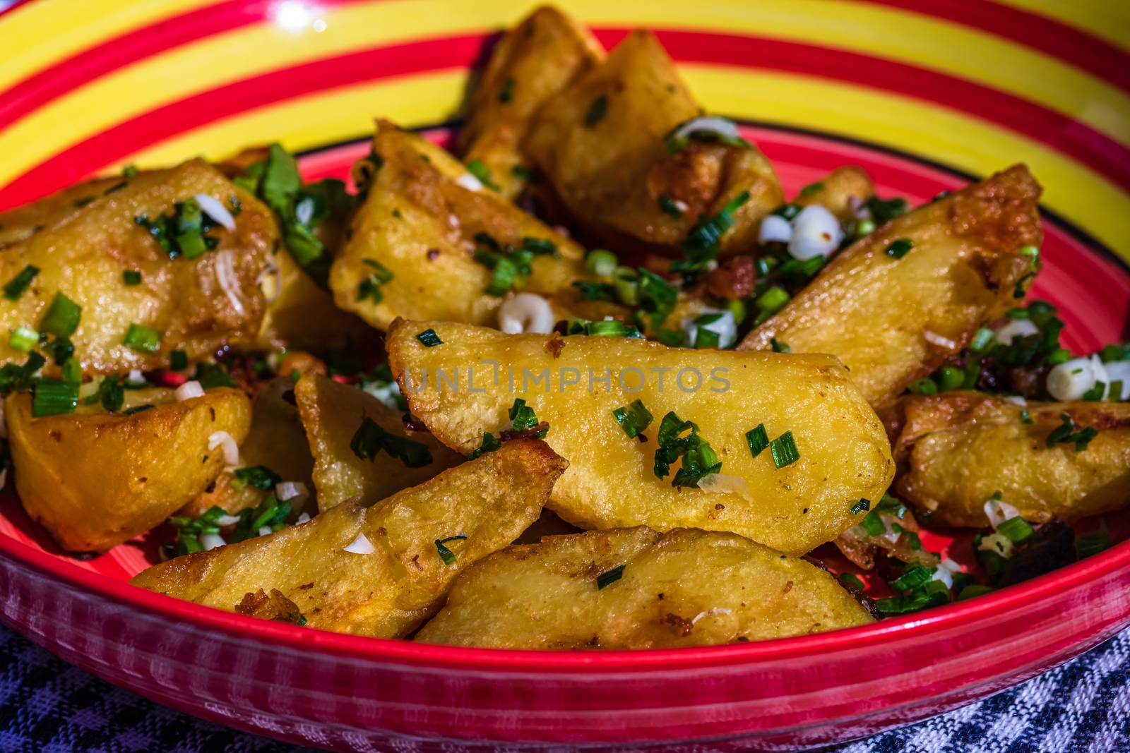 Close up with selective focus of fried potatoes with green onion, green garlic and spices in a colorful plate.