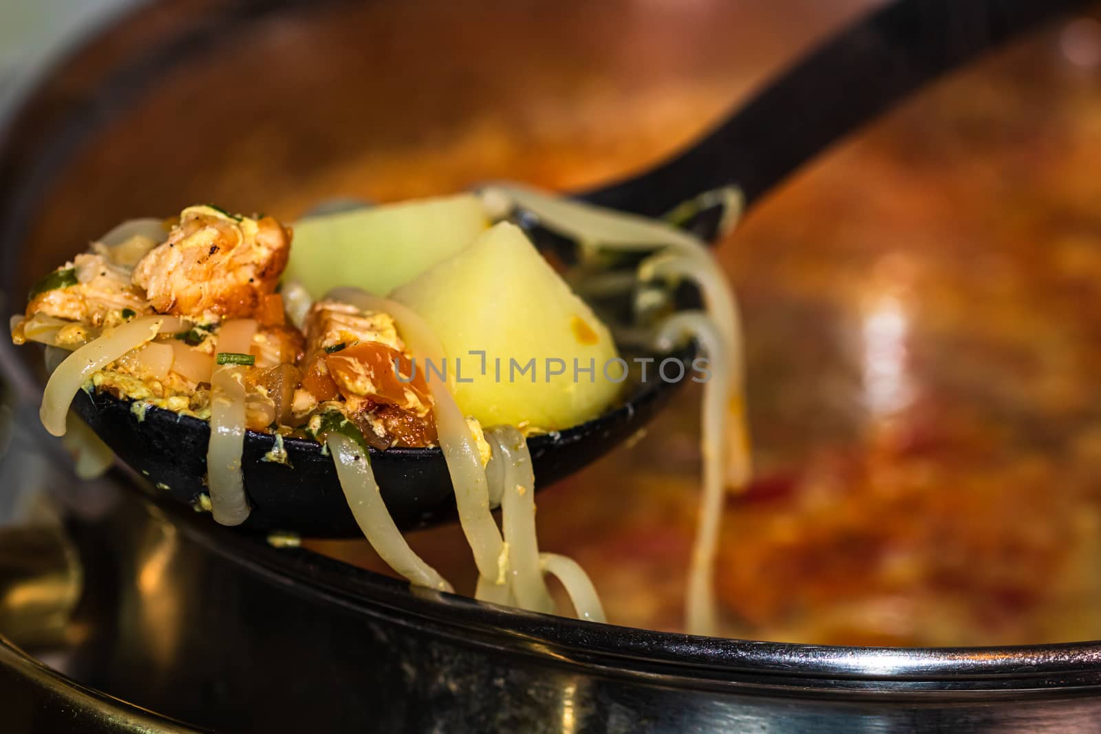 Preparation of soup with chicken and vegetables. Close up of boiling soup, focus on spoon with noodles and vegetables.