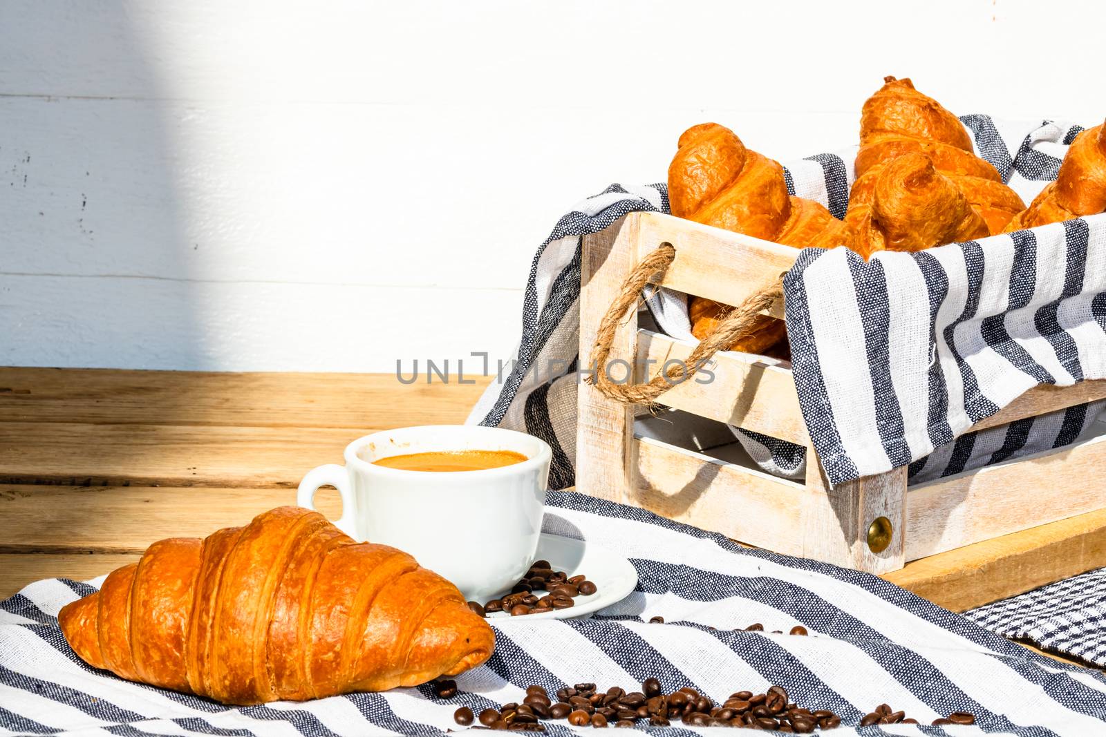 Puff pastry, coffee cup and buttered French croissant on wooden crate. Food and breakfast concept. Detail of coffee desserts and fresh pastries