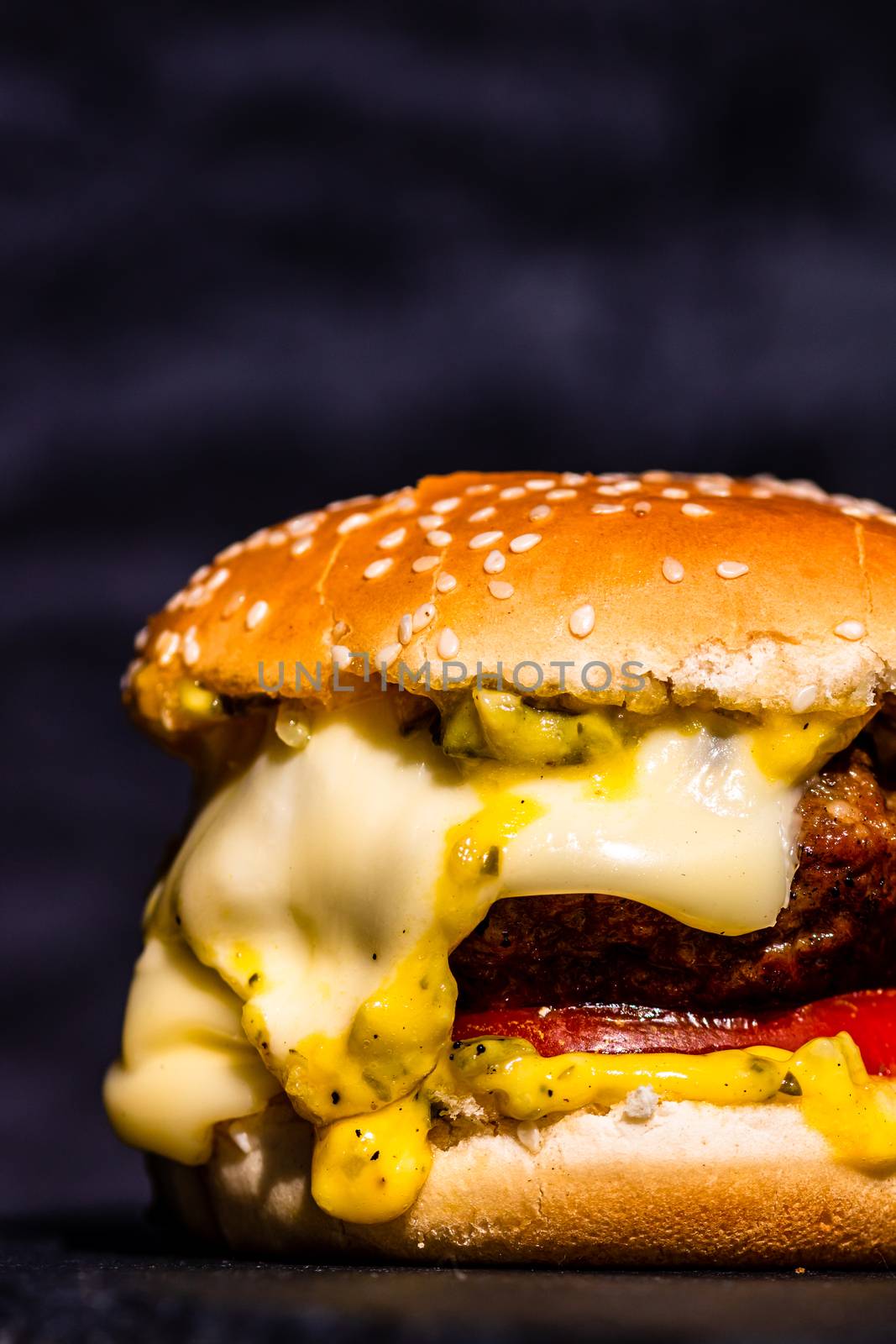 Detail of beef cheeseburger with melted cheese isolated on black background.