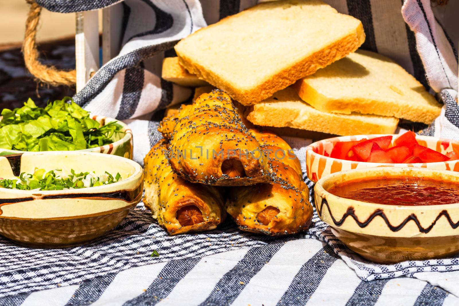 Sausages baked in dough sprinkled with salt and poppy seeds in a rustic composition. Sausages rolls, delicious homemade pastries.