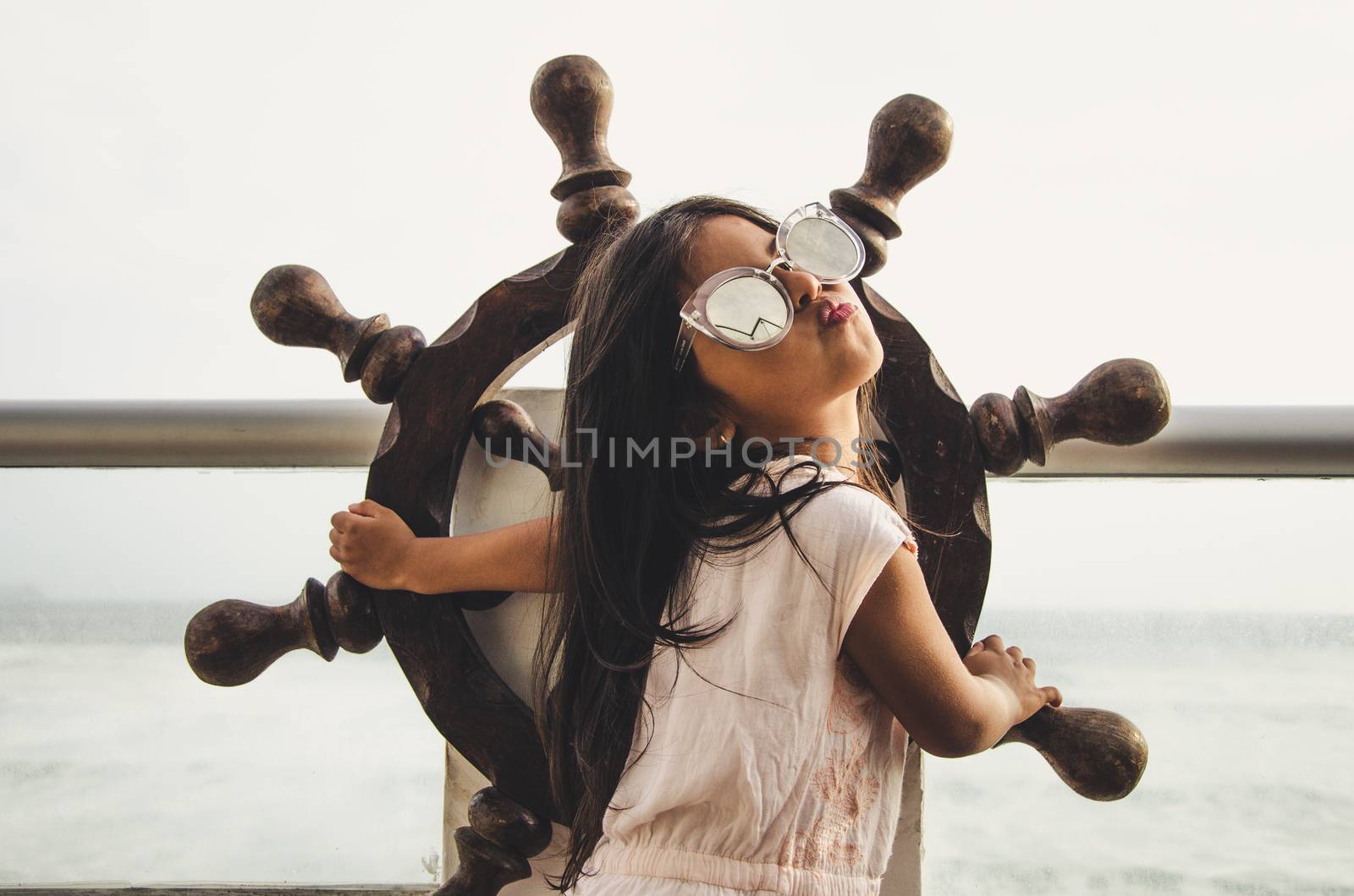 Little girl playing to be a sailor on a balcony with a boat rudder and the background of the sea