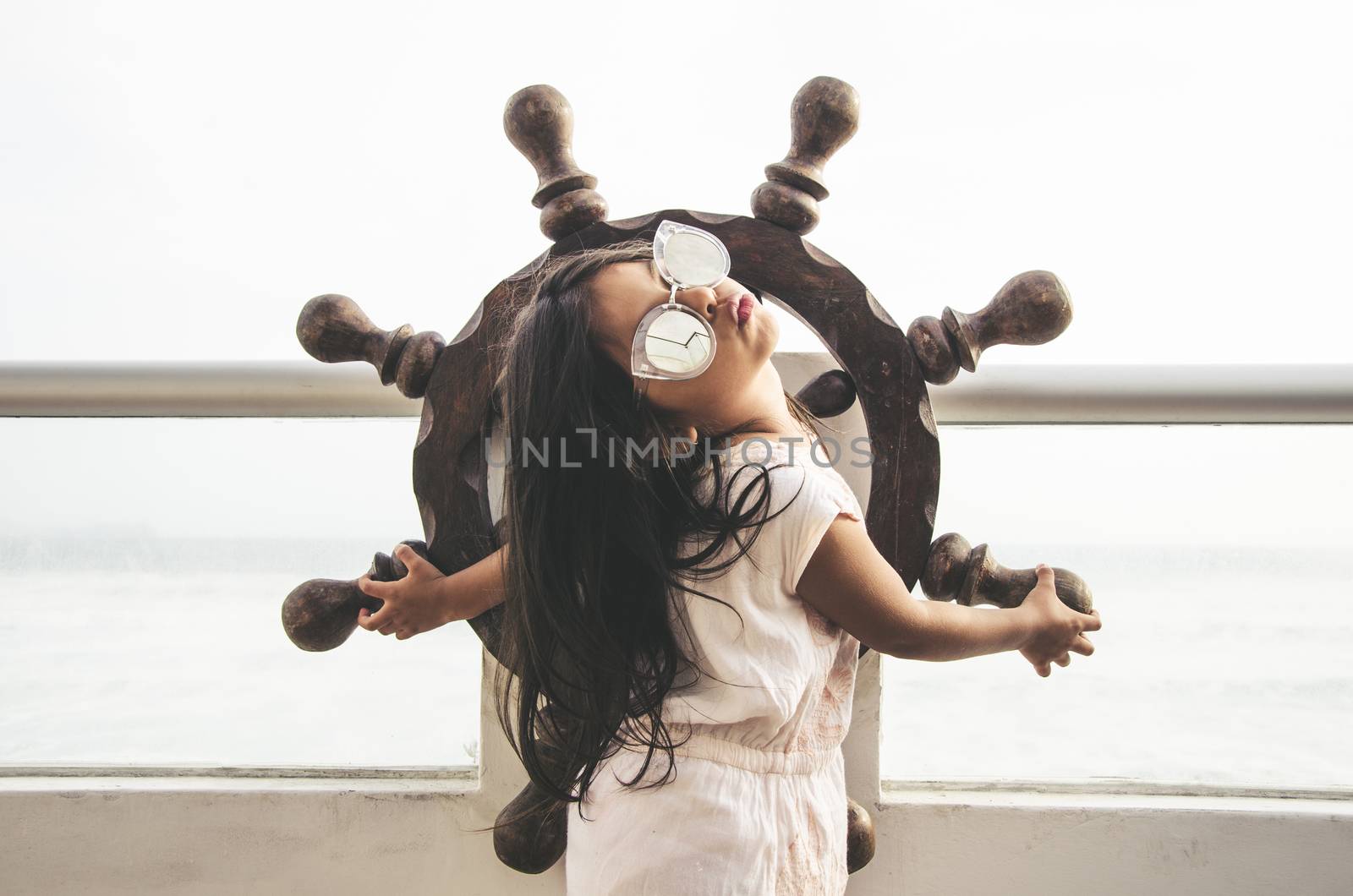 Little girl playing to be a sailor on a balcony with a boat rudder and the background of the sea