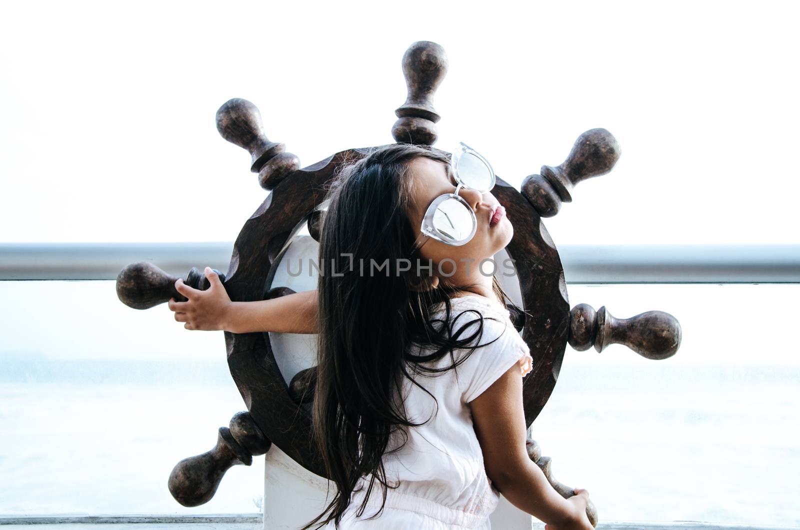 Little girl playing to be a sailor on a balcony with a boat rudder and the background of the sea