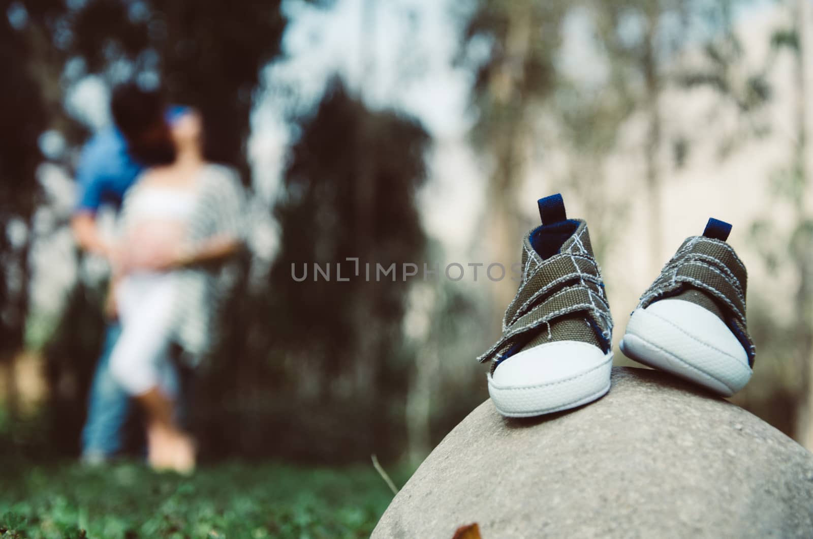 Baby slippers on a stone, with a background of parents embraced and blurred nature