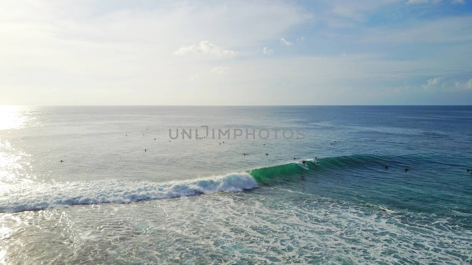 Surfers catch waves at Uluwatu beach, Bali. Huge waves stretch along the beach. A lot of people with boards are catching waves. The wave swirls into the tube, a huge foam. View from a drone.