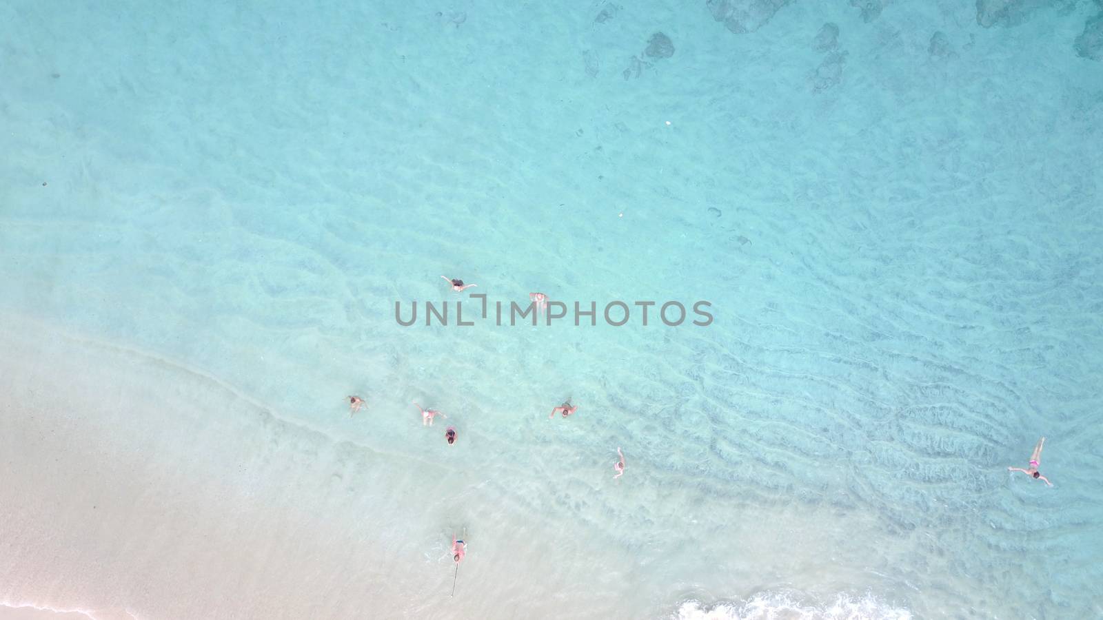 White sand and turquoise clear water on the beach. People are swimming among the waves. The view from the top. The sand is black in places. The bottom is completely visible. island of Bali.