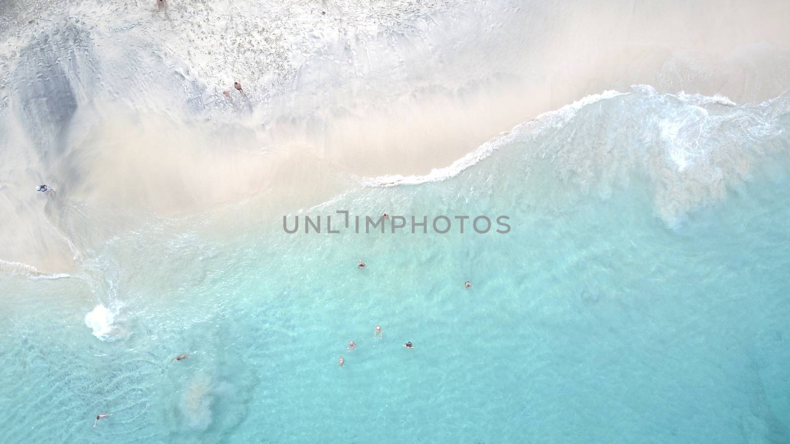 White sand and turquoise clear water on the beach. People are swimming among the waves. The view from the top. The sand is black in places. The bottom is completely visible. island of Bali.