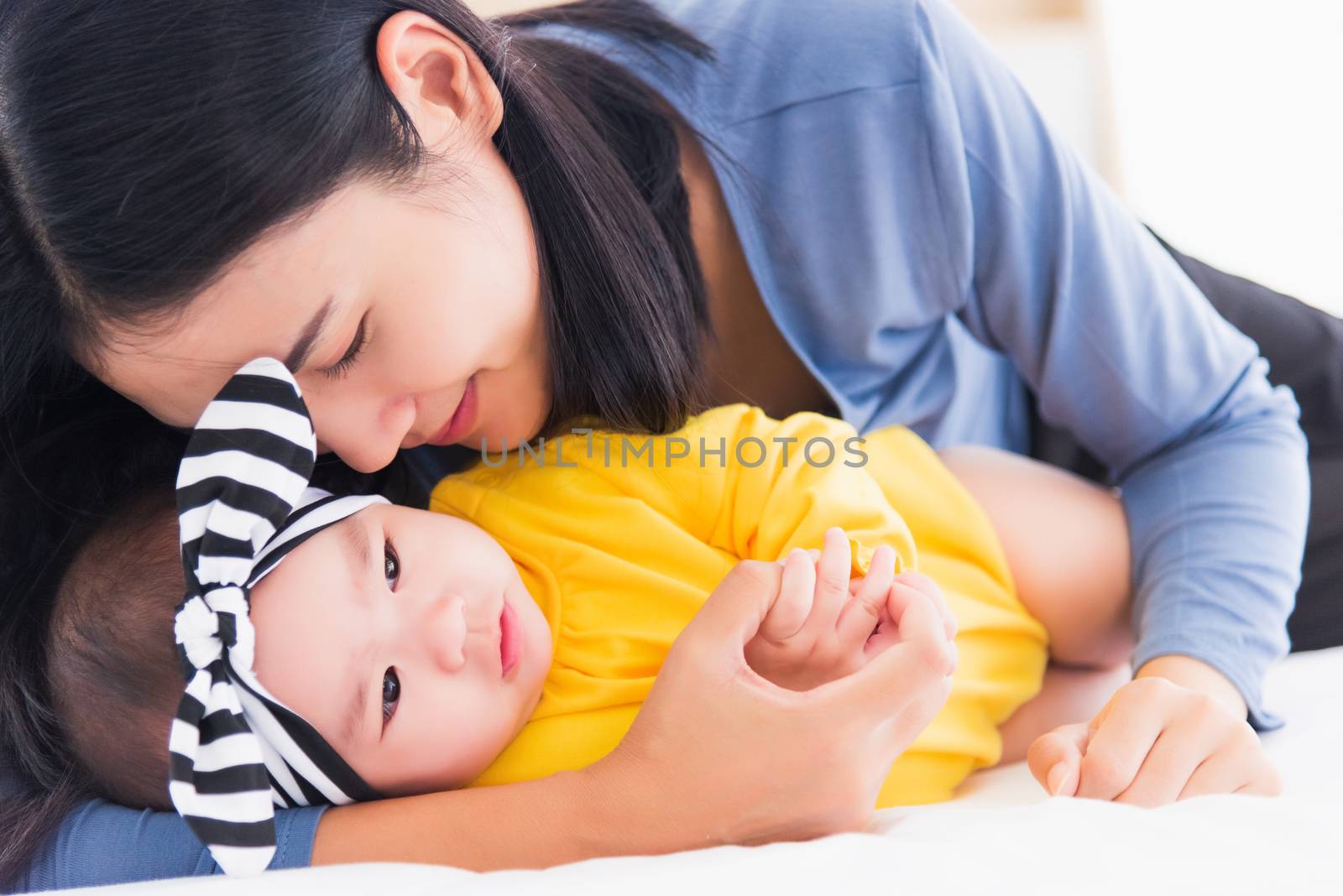 mother kissing her infant newborn baby in a white bed by Sorapop