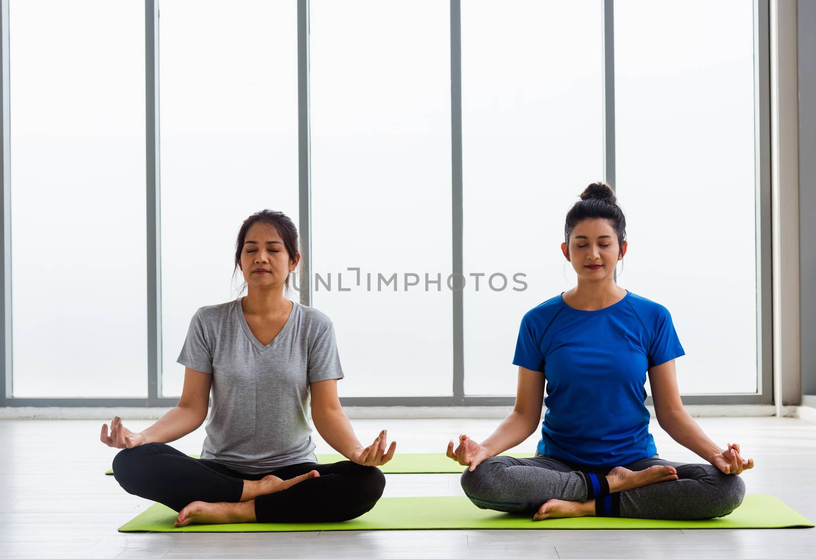 Two Asian women sporty attractive people practicing yoga lesson  by Sorapop