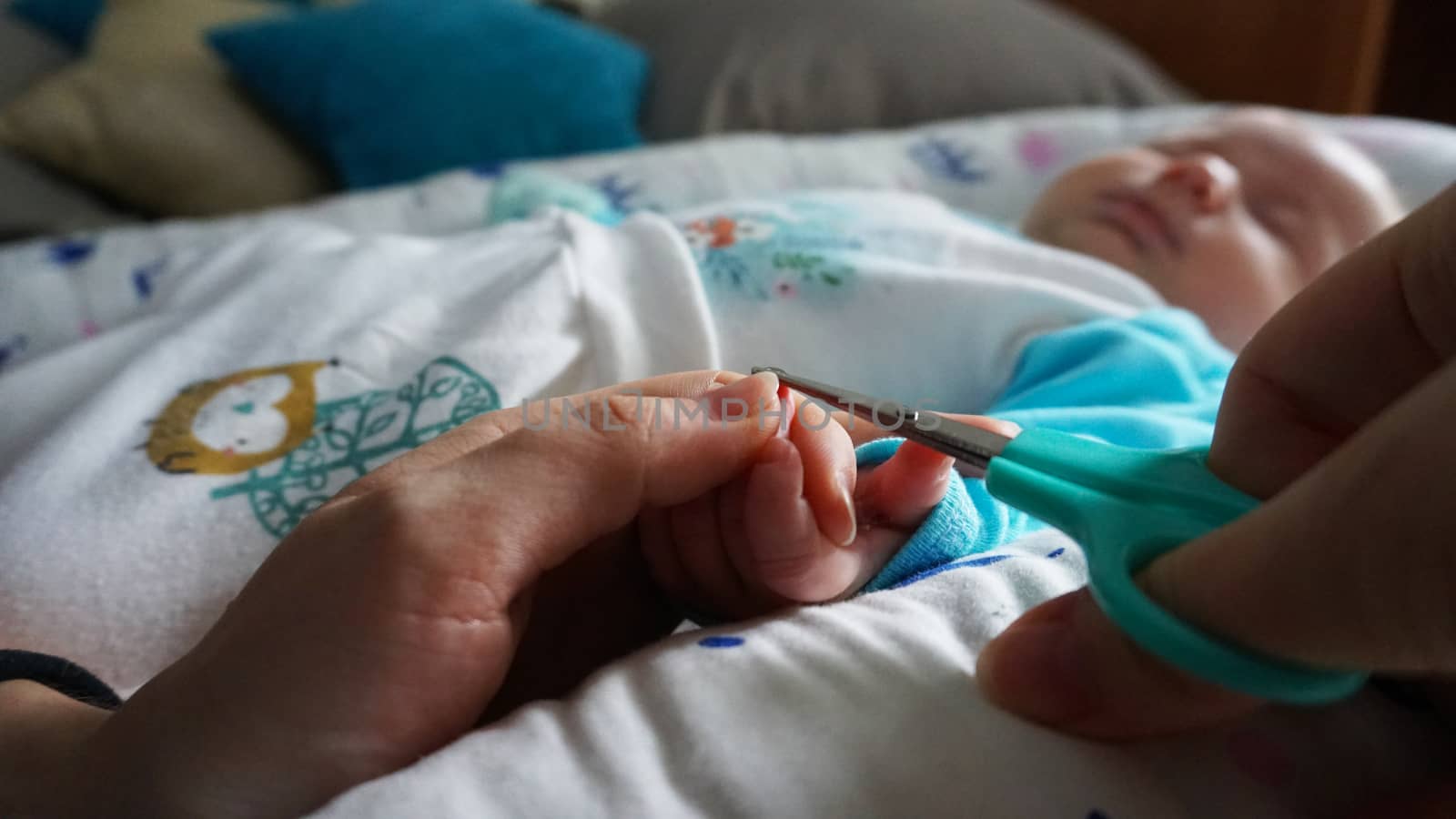 A newborn child's nails are cut with special baby scissors. An adult hand holds a small child's hand. Carefully, the mother cuts her daughter's nails. A child in a cocoon, home environment. Trust.