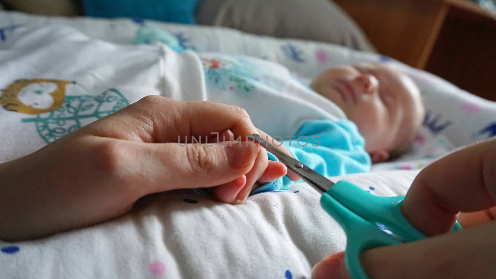 A newborn child's nails are cut with special baby scissors. An adult hand holds a small child's hand. Carefully, the mother cuts her daughter's nails. A child in a cocoon, home environment. Trust.