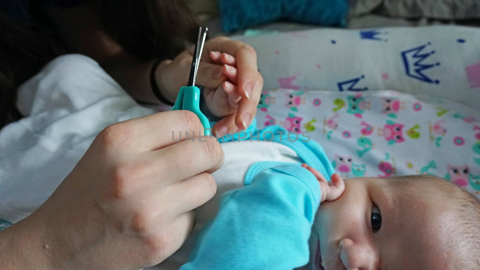 A newborn child's nails are cut with special baby scissors. An adult hand holds a small child's hand. Carefully, the mother cuts her daughter's nails. A child in a cocoon, home environment. Trust.
