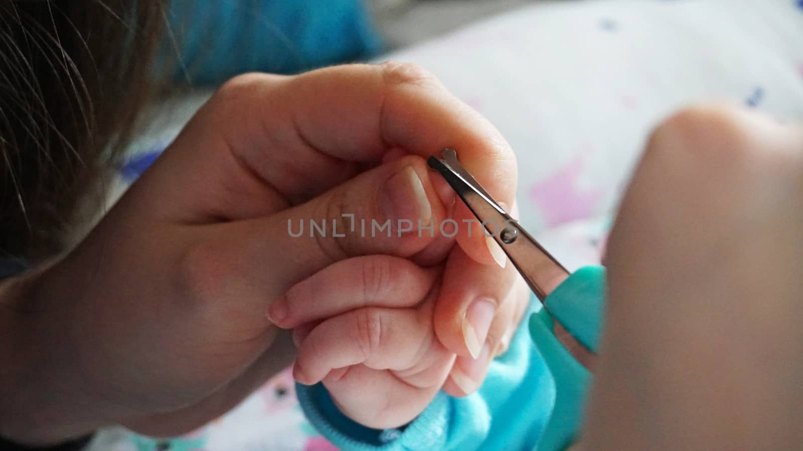 A newborn child's nails are cut with special baby scissors. An adult hand holds a small child's hand. Carefully, the mother cuts her daughter's nails. A child in a cocoon, home environment. Trust.