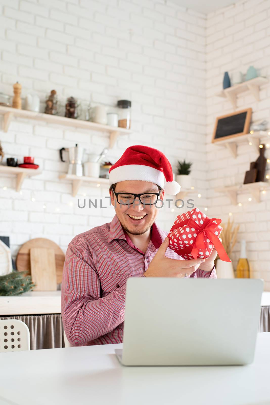 Happy young man in santa hat greeting his friends in video chat or call on laptop by Desperada
